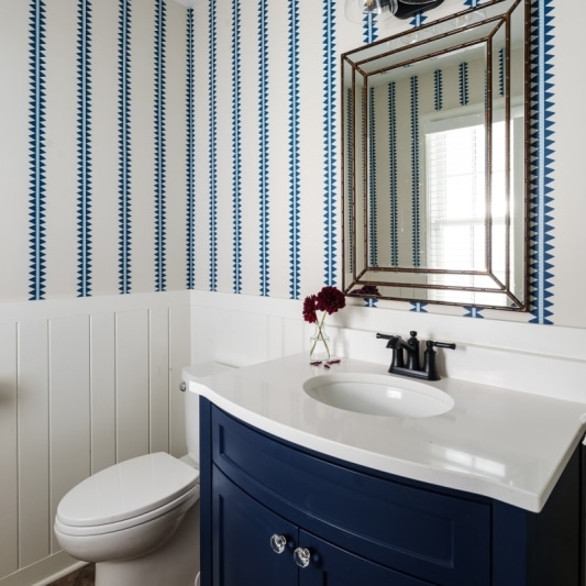 Coastal vibes in this powder bath with blue and white wallpaper and dark blue wood vanity