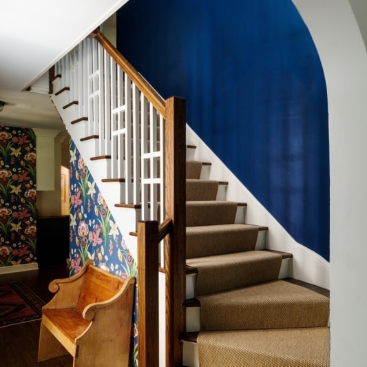 wallpapered hallway and navy blue wall up the newly refinished stairway