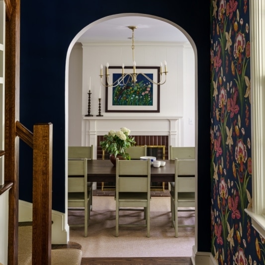 dining room shot through the arched doorway, navy floral wallpaper and light sage green chairs