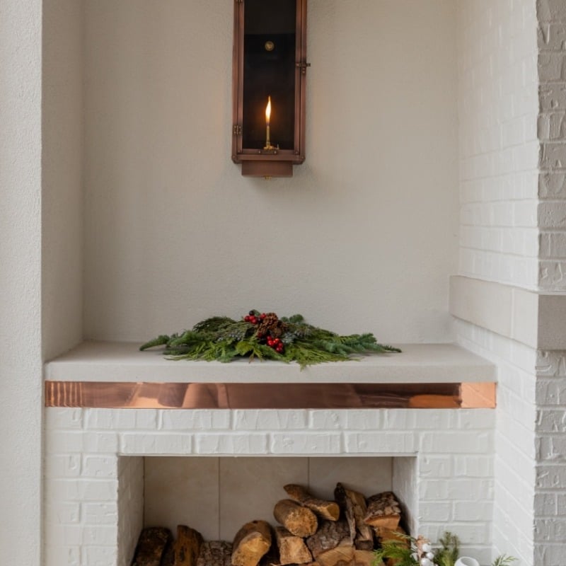 Detail shot of the brick work and built-in wood storage near the fireplace with a gas burning light fixture and christmas or holiday greenery for decor