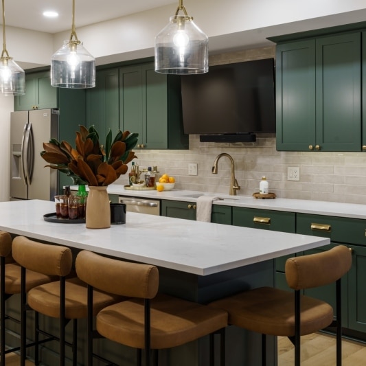 Basement with dark green kitchen cabinets, 3 island pendants, and carmel leather stools