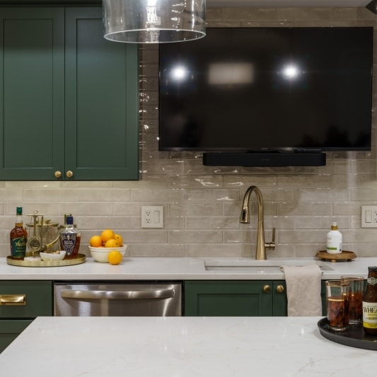 Green basement kitchen with mounted tv, beverage fridge, and tile backsplash