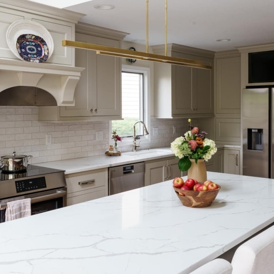 A bright and airy kitchen with light cabinets, a large island with a white countertop and seating, stainless steel appliances, and pendant lighting.