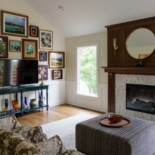 A living room featuring a fireplace with a herringbone tile surround, a dark wood mantel, and a gallery wall filled with framed artwork.