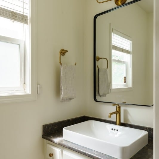 modern powder bath with white sink and black counters and gold hardware