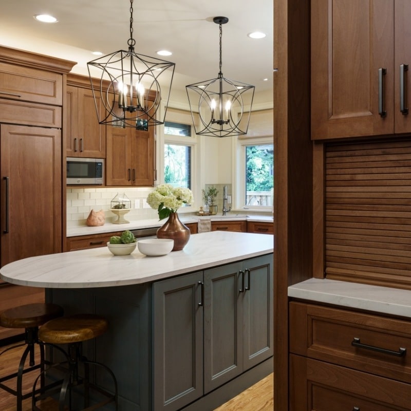A modern kitchen with a gray island, white countertop, and warm wood cabinetry.