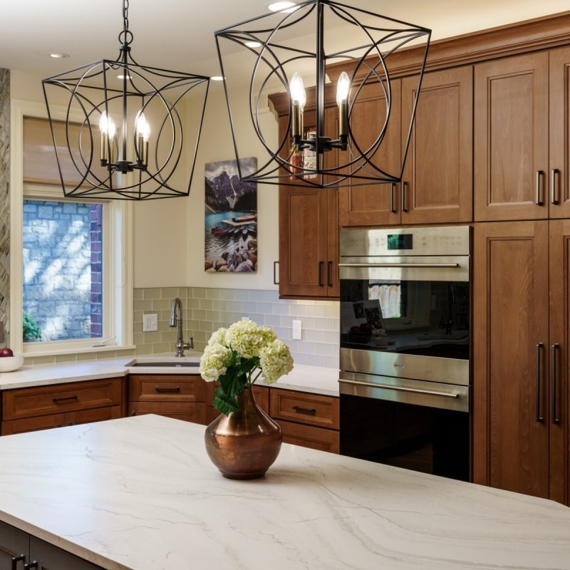 A beautifully remodeled kitchen featuring warm wood cabinets, a large curved white countertop island with seating, a decorative range hood, and modern pendant lighting.