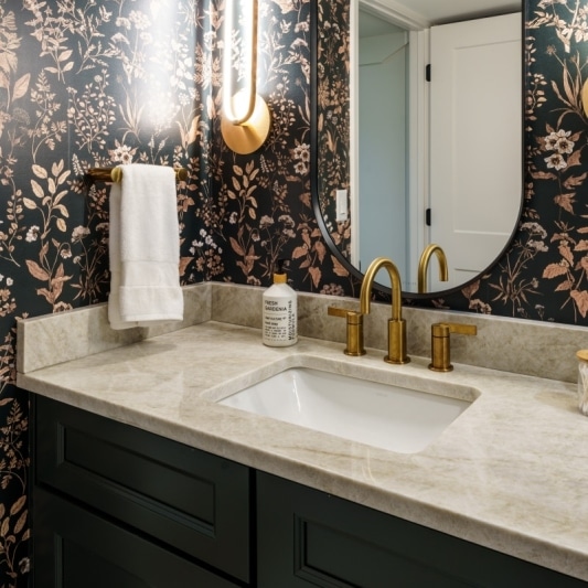 Bathroom with floral wallpaper, oval mirror and light fixtures, and brass faucet