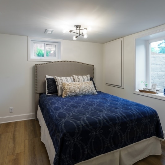 Basement bedroom with egress window and bed with blue comforter
