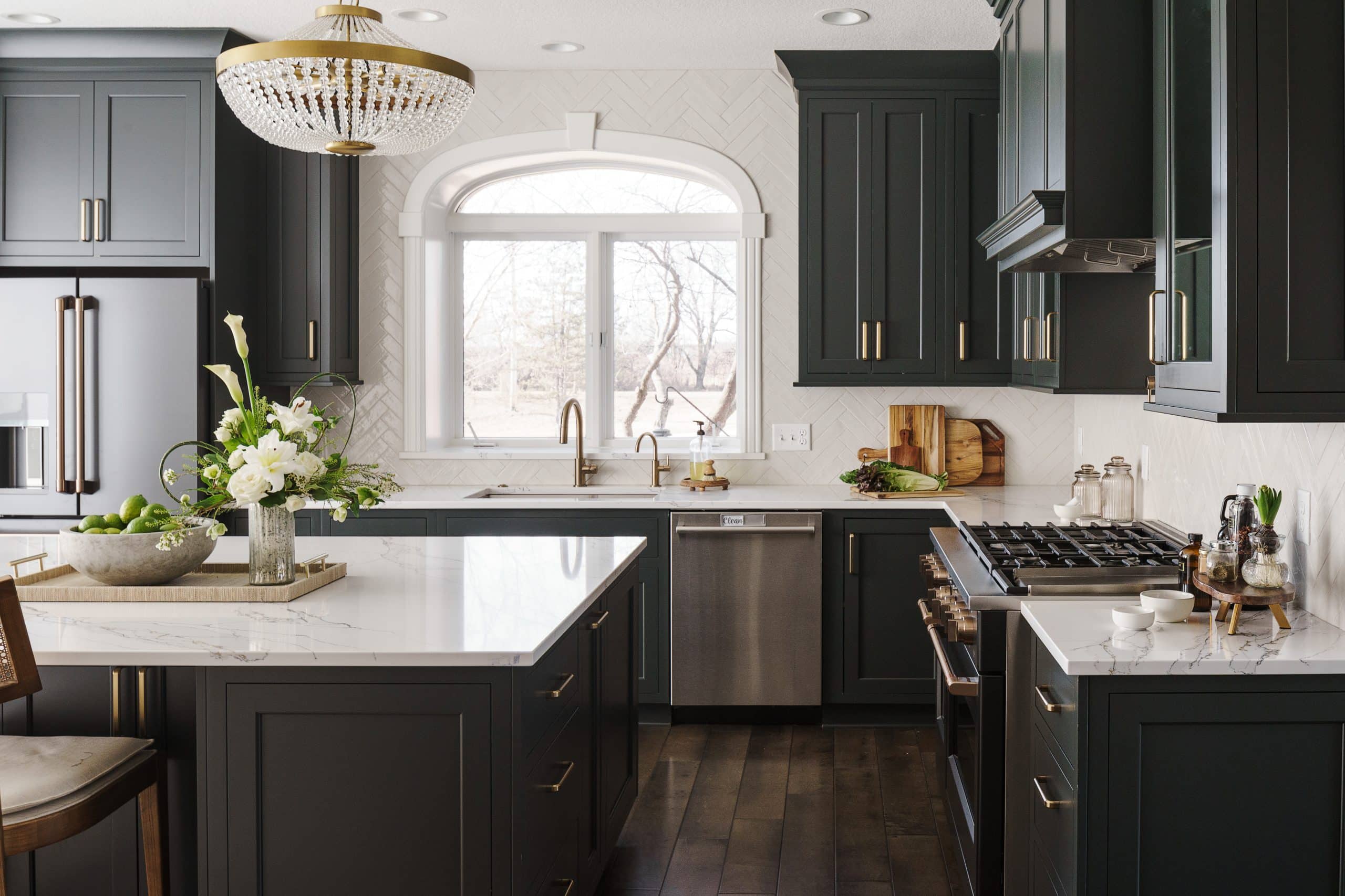 Luxurious dark green kitchen remodel Overland Park KS with marble countertops, gold accents, and crystal chandelier.
