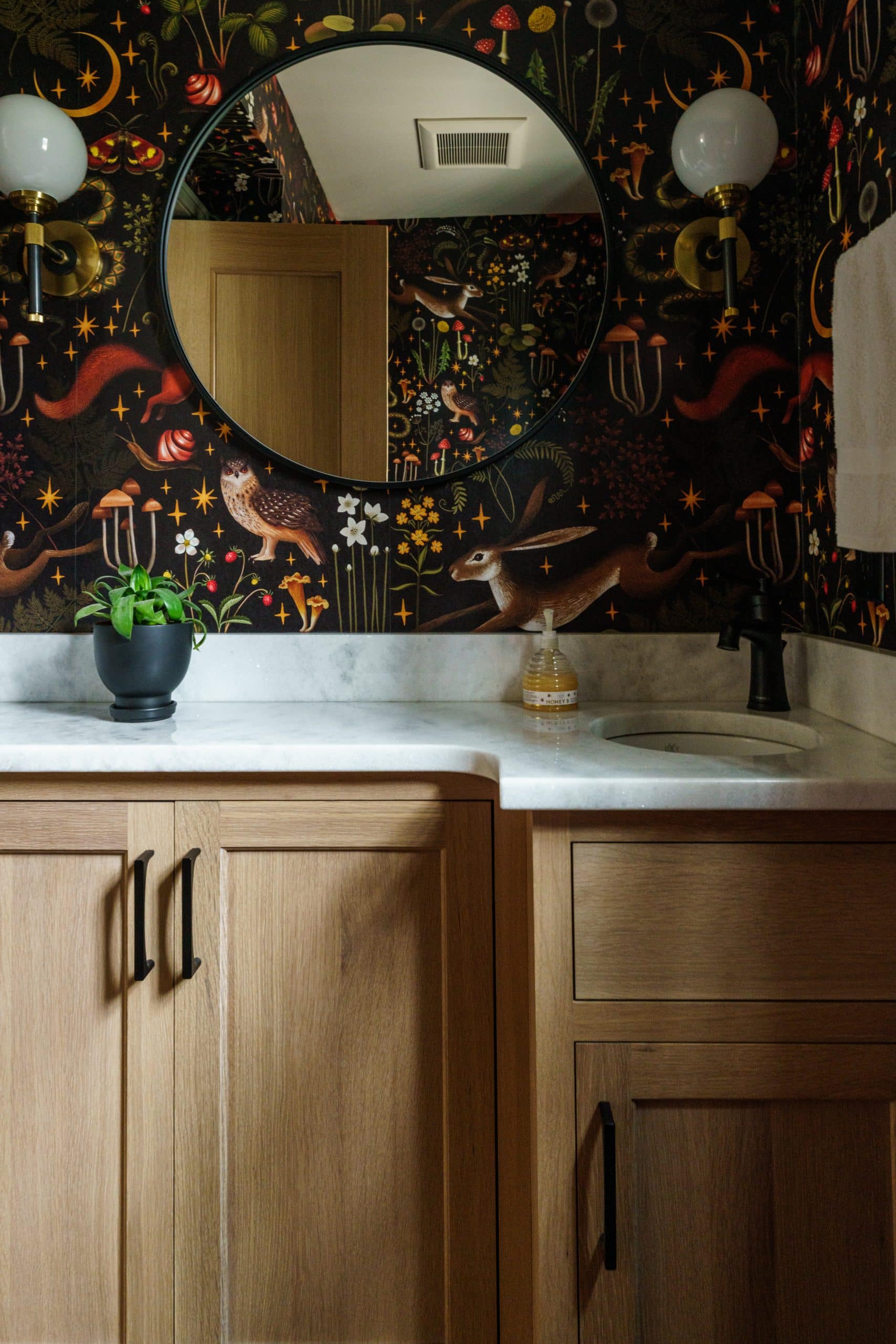 whimsical wallpaper and light oak powder bath with bright white counter tops. It's a spot full of charm and character.