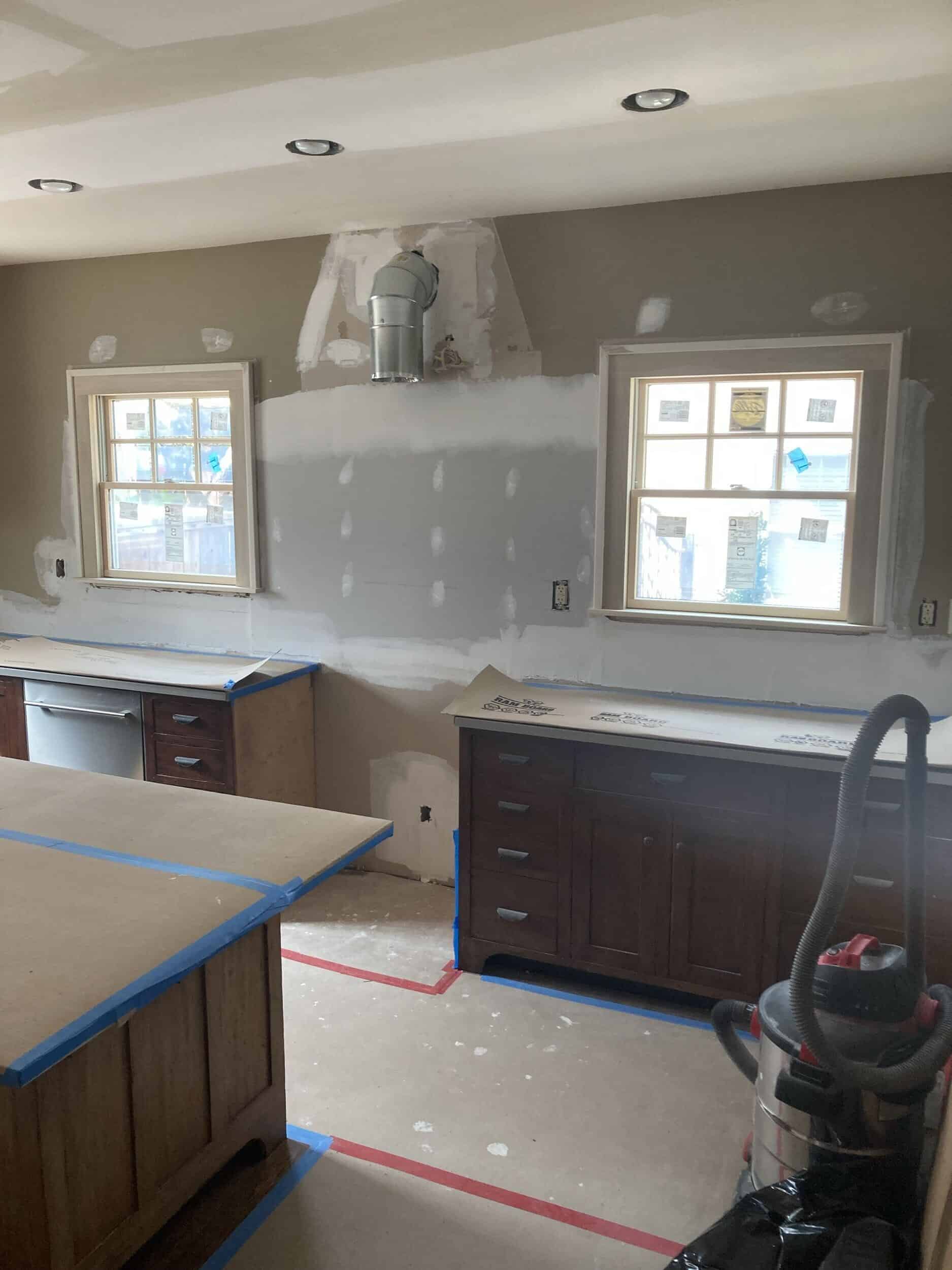 drywall is hung and holes have been patched over getting the walls ready and prepped for tile backsplash to be layed over top. You can see the whole kitchen from this angle.