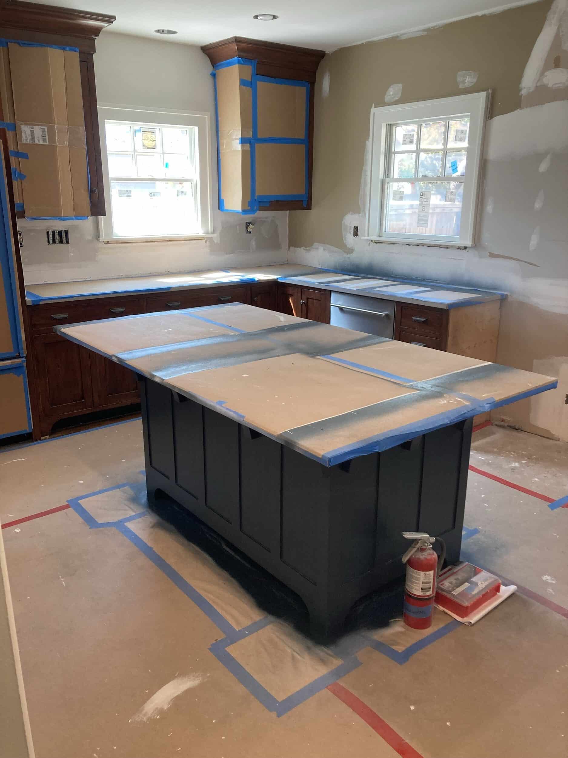 We used a paint sprayer to make the kitchen island cabinetry Sherwin Williams Sea Serpent a dark moody deep blue with green undertones. the rest of the kitchen is taped off and covered so it doesn't get paintd