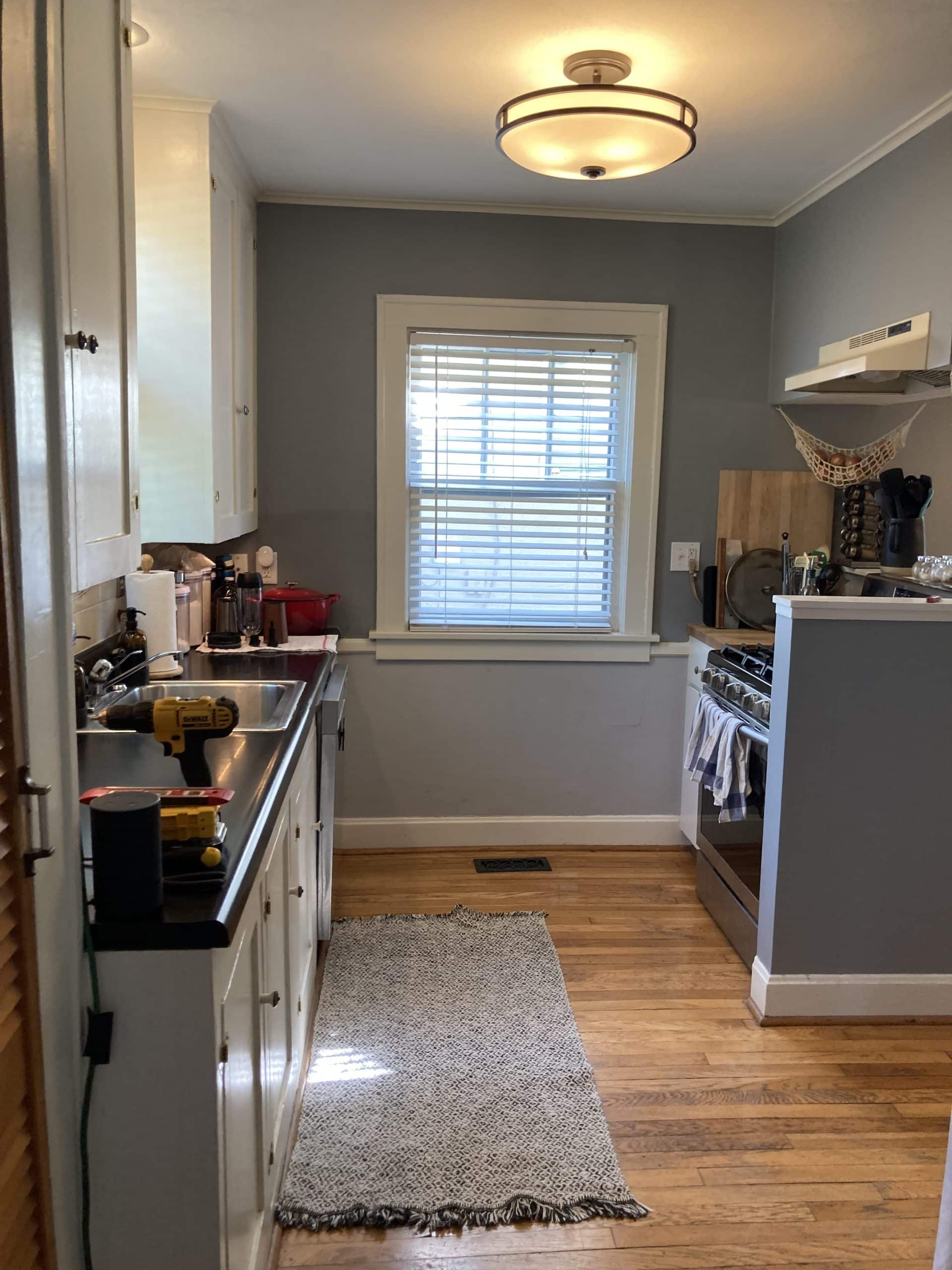 brookside revival project before image of small crammed and very dated kitchen. a sort of galley kitchen with blue gray walls and dark counters. very minimal storage is present