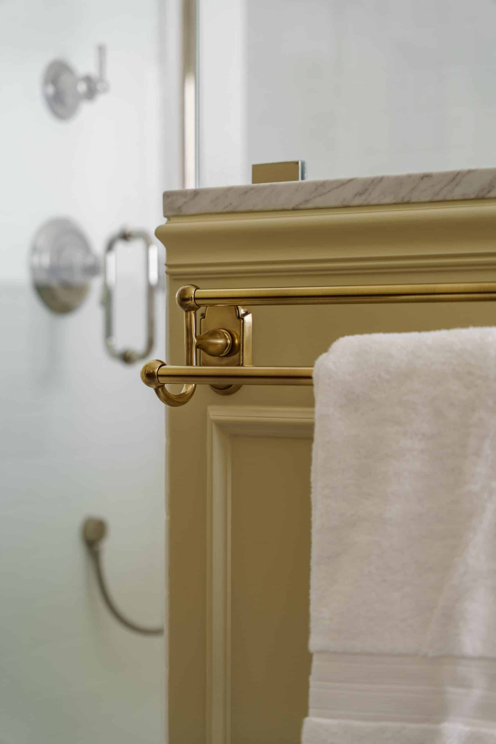 Detail shot of a classic brass wall-mounted towel bar, part of the elegant fixtures in a primary bathroom remodel, positioned next to a wainscoted partition
