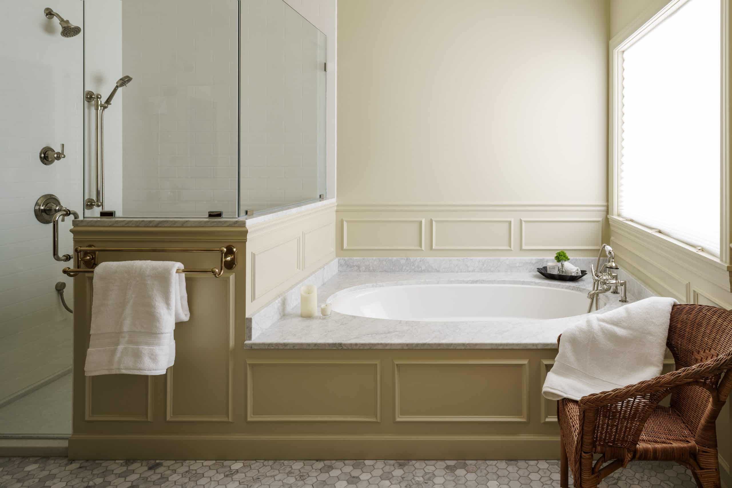 Close-up of a primary bathroom remodel, detailing a classic undermount soaking tub set into a marble counter, complemented by rich wainscoting on the tub surround and walls, with a glass shower enclosure visible on the left