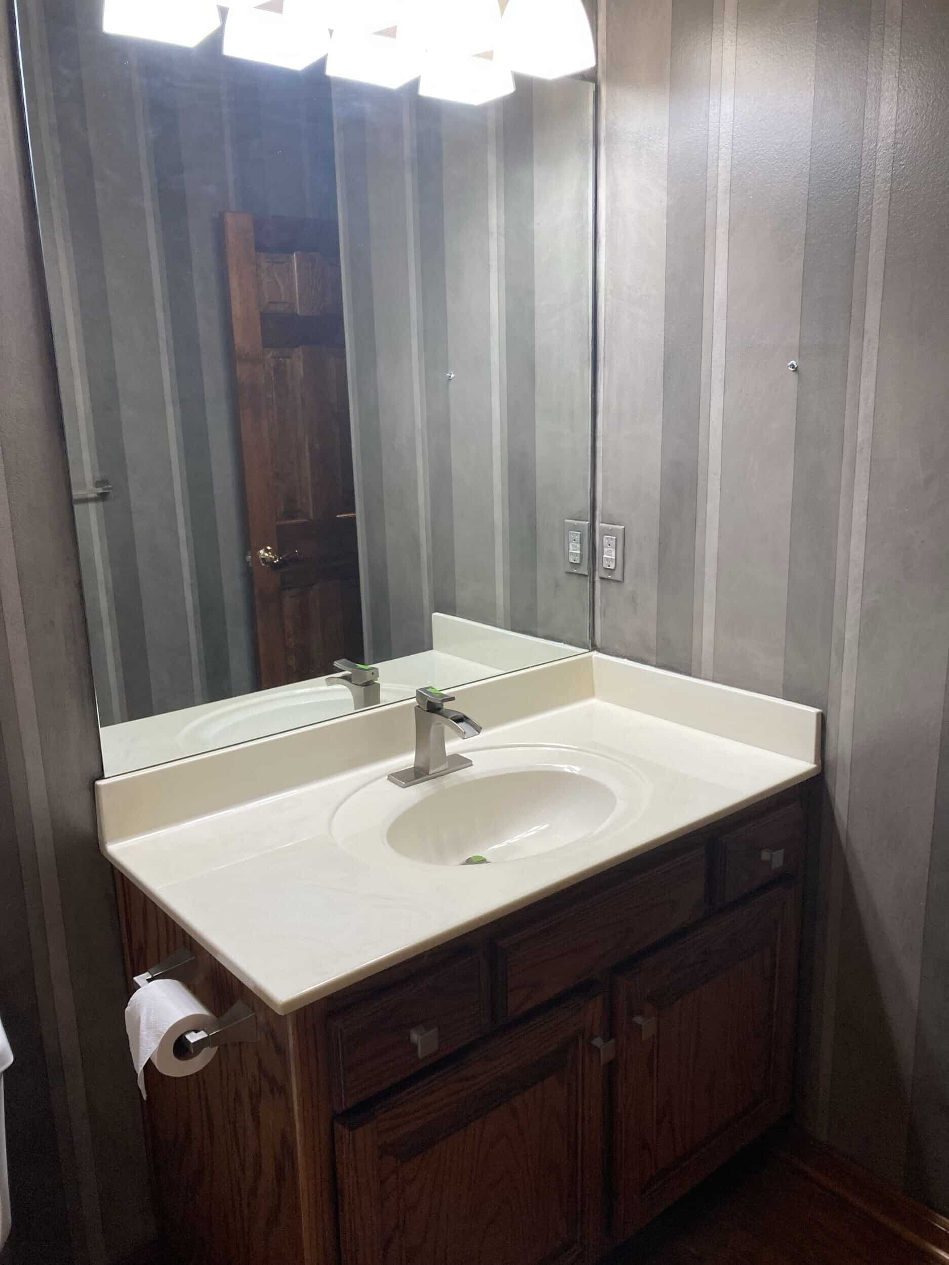 hall bath before demo featuring dark wood floors and dark vanity and dark dated wallpaper
