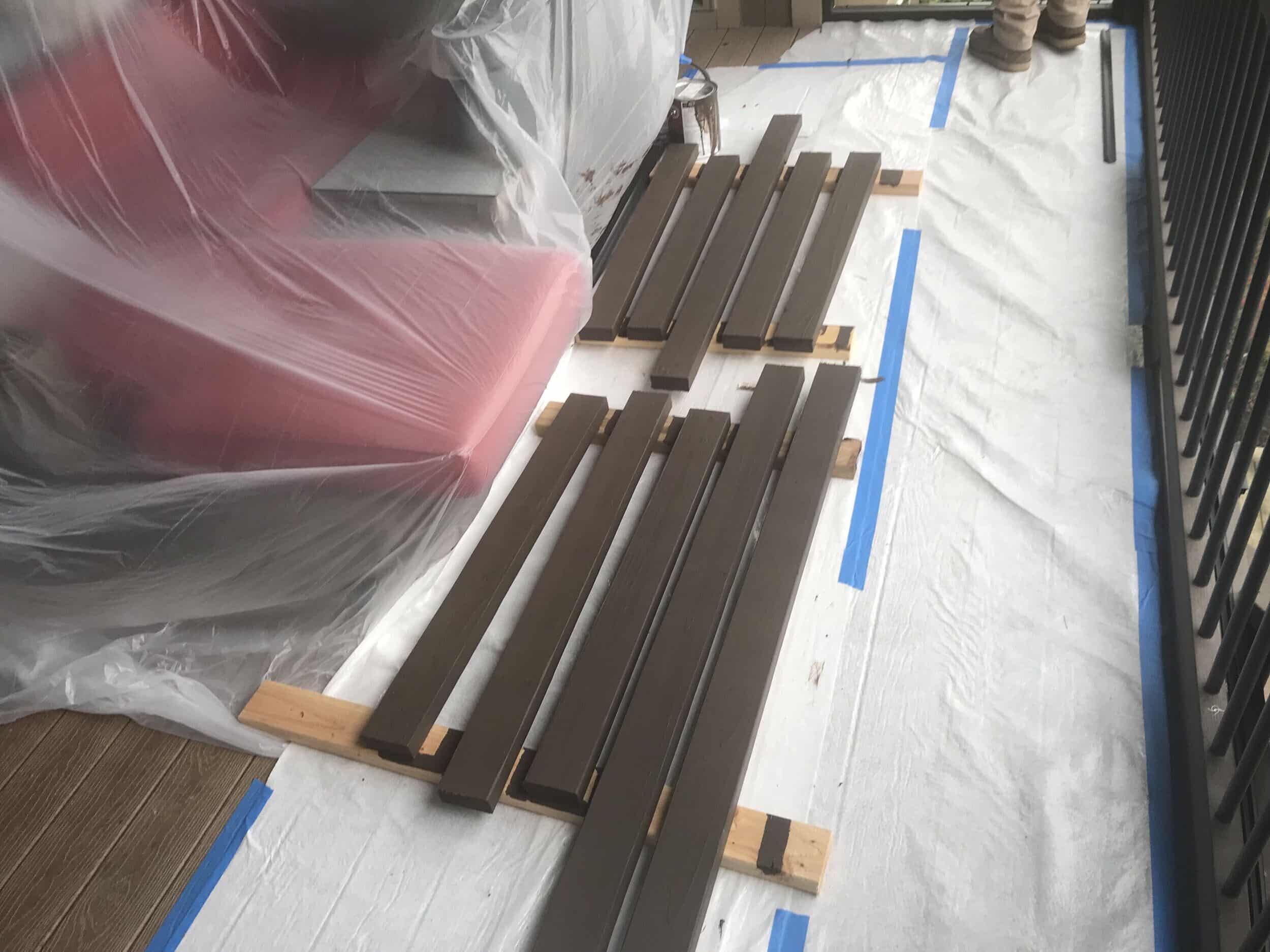 fresh cut trim pieces laid on floor in short lengths with a dark brown wet stain still drying before they can be hung