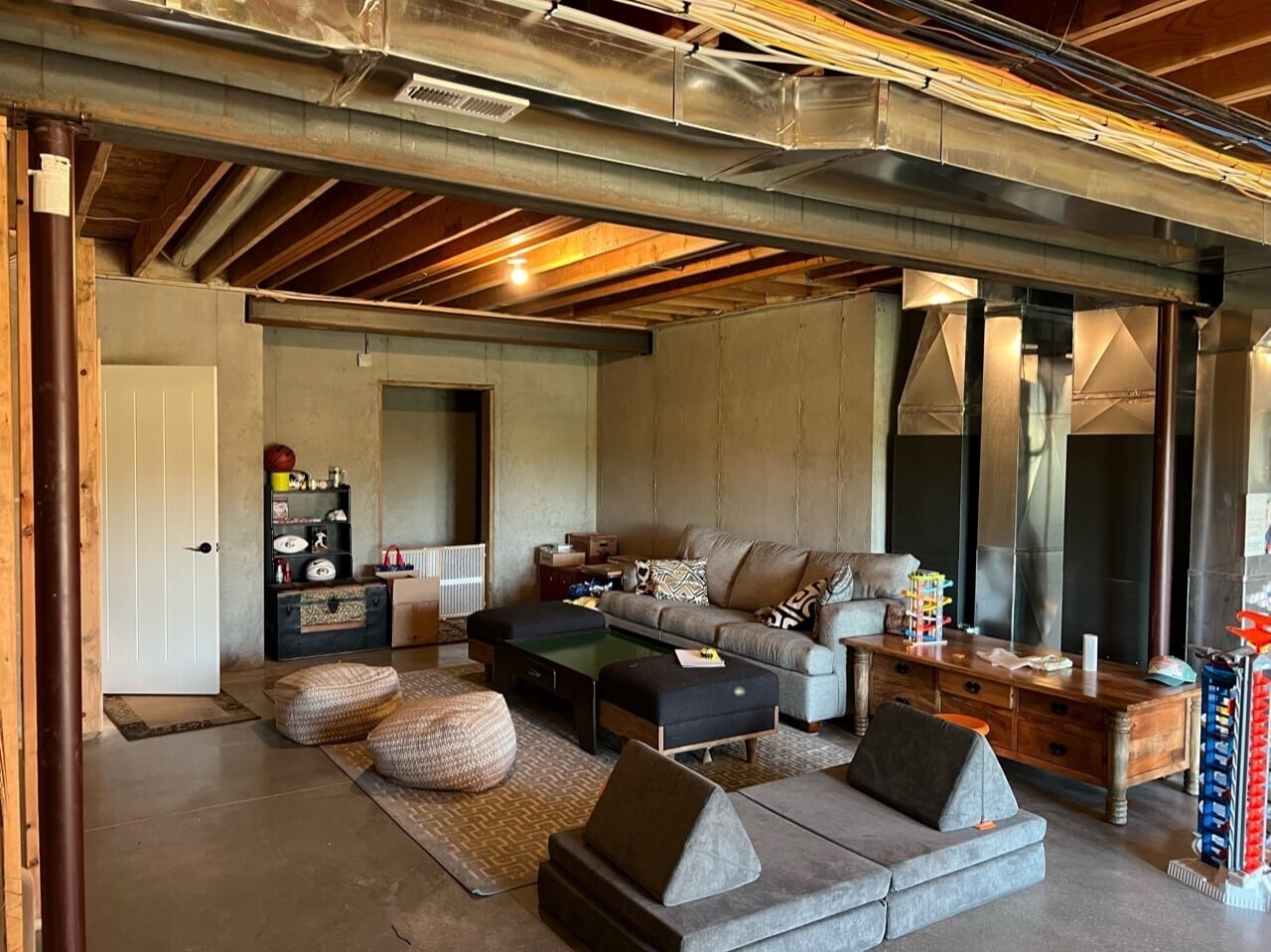 basement before the remodel, bare with concrete and exposed pipes duct work and wires