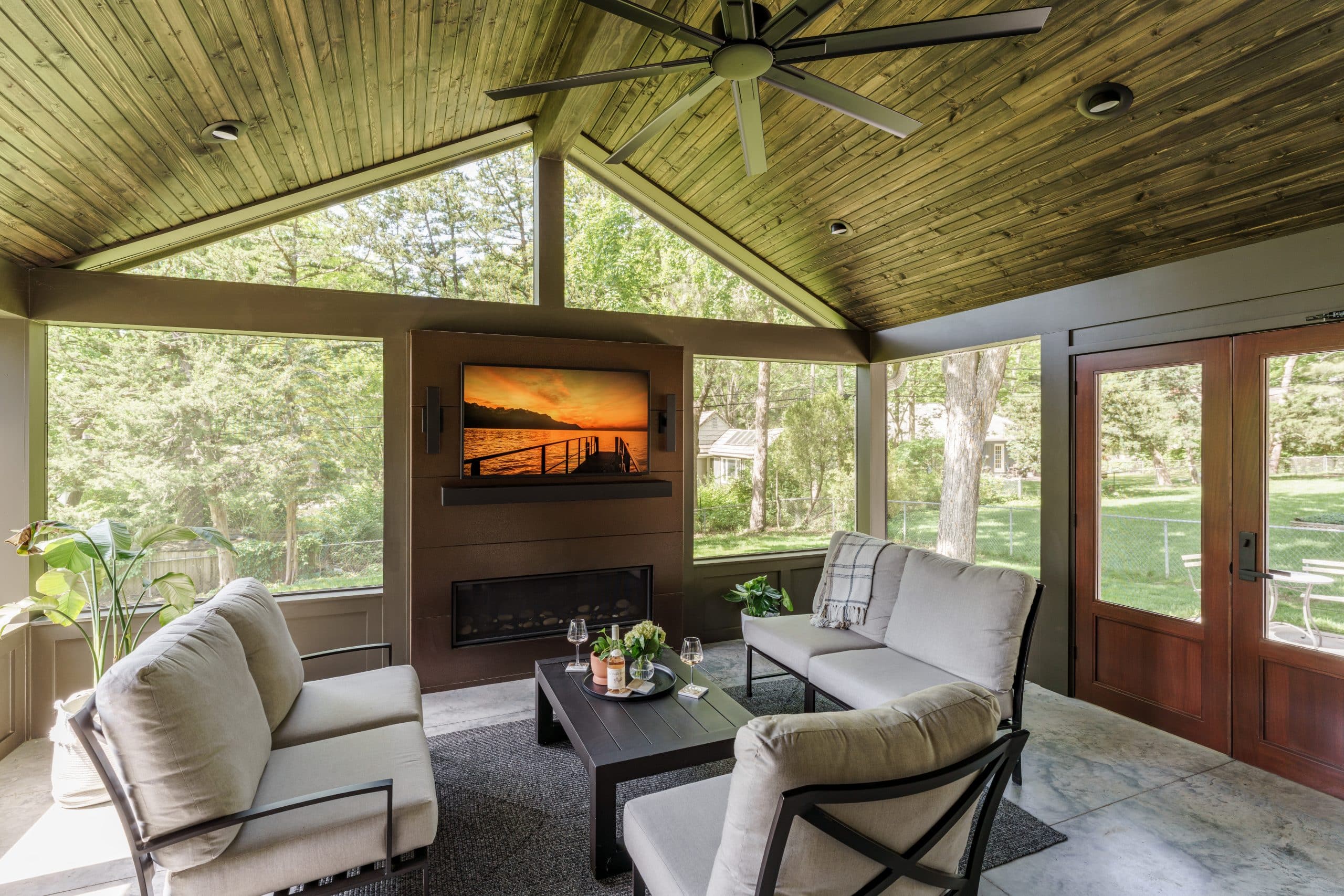A view from inside a remodeled screened porch, showcasing the large glass French doors that lead into the main house and the bright, comfortable seating area