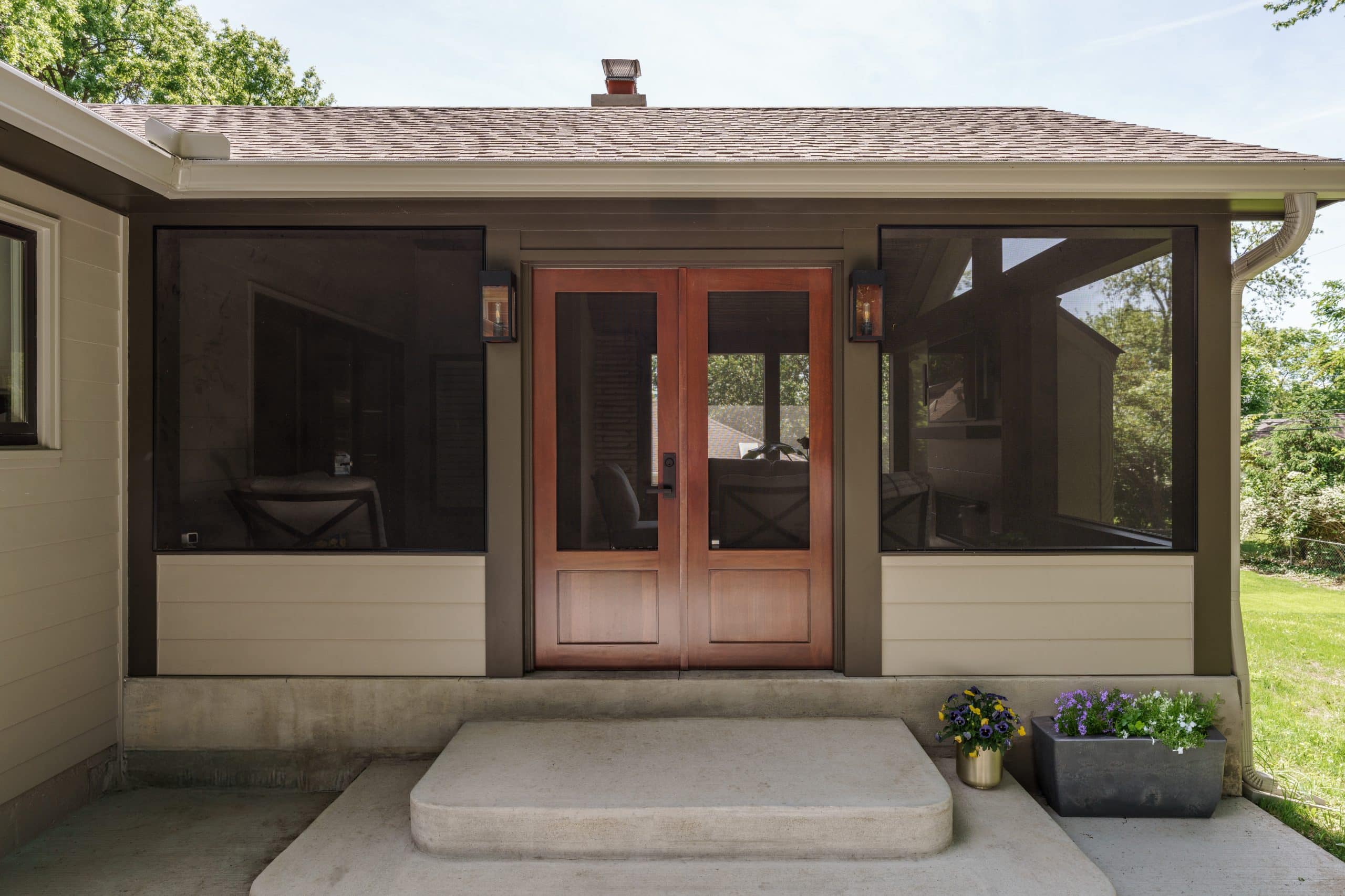 Modern screened porch exterior with dark brown screens, a light-colored siding, and double wooden entry doors, seamlessly integrated into an existing ranch-style home