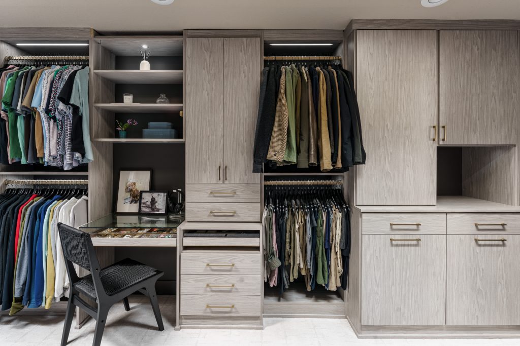 This image captures the incredible detail and custom functionality of this Overland Park closet transformation. The photo highlights the dedicated vanity and accessory area, designed for a seamless getting-ready routine. With a clear glass top, the drawers beautifully display jewelry and watches, while open shelving provides space for décor and personal items. Every element, from the custom cabinetry to the elegant gold hardware, was chosen to create a space that is both highly organized and beautifully luxurious