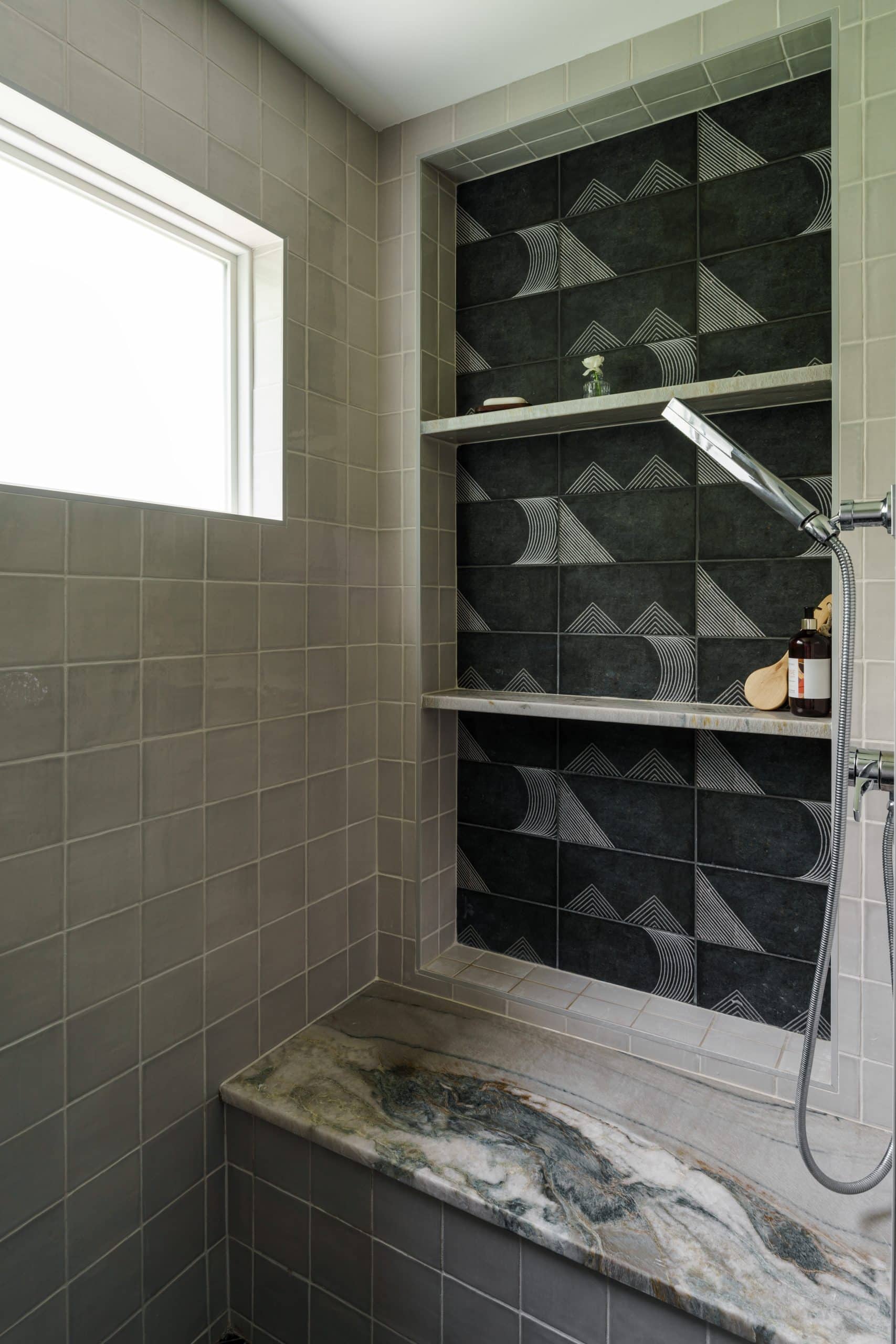 Modern walk-in shower design featuring gray matte subway tile walls, a dramatic gray-veined natural stone shower bench, and a recessed niche with black and white patterned accent tile.