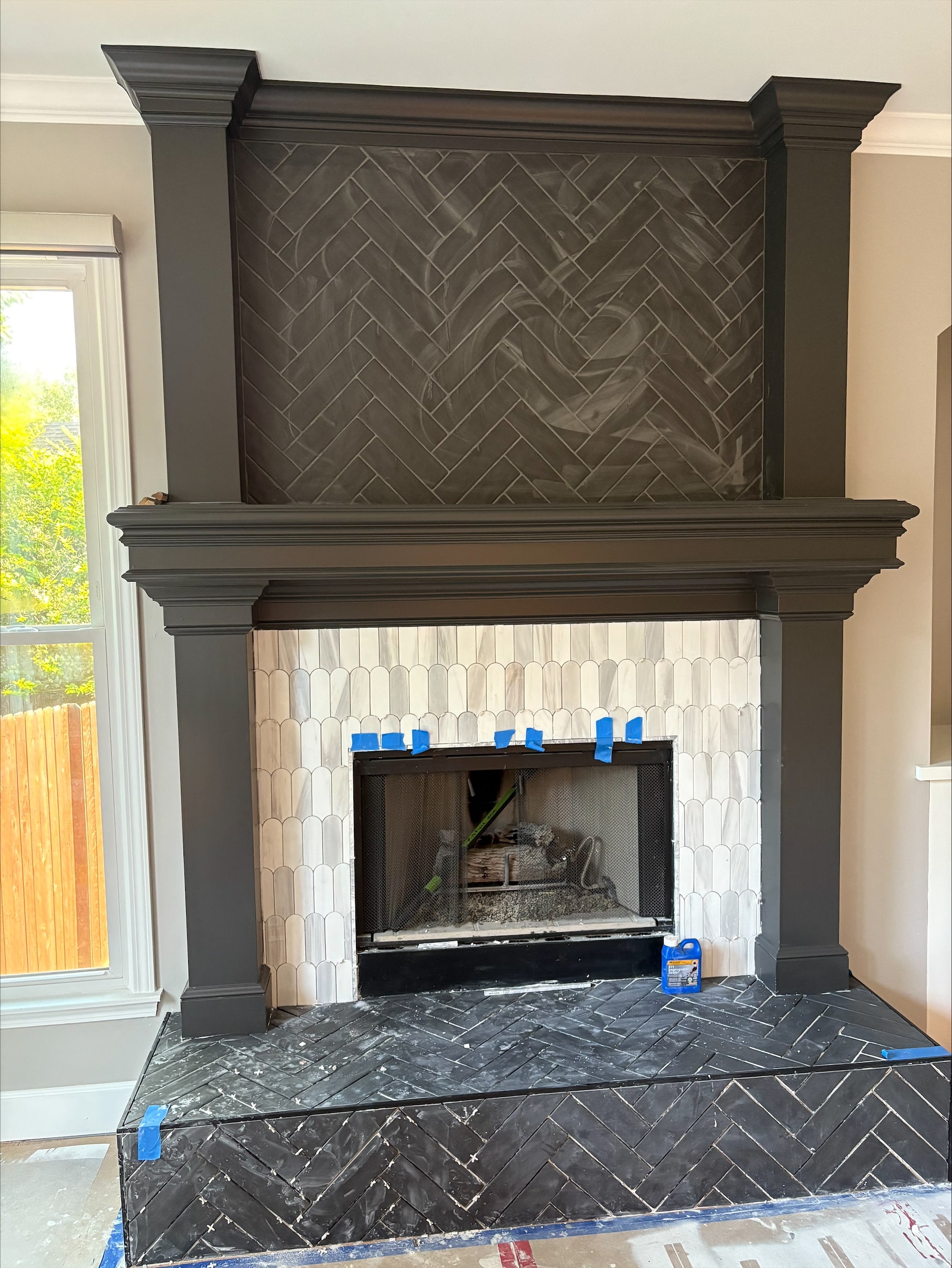 black matte black brick looking tile laid in a herringbone pattern on the fire place and a white marble scallop tile in the middle area to add some contrast