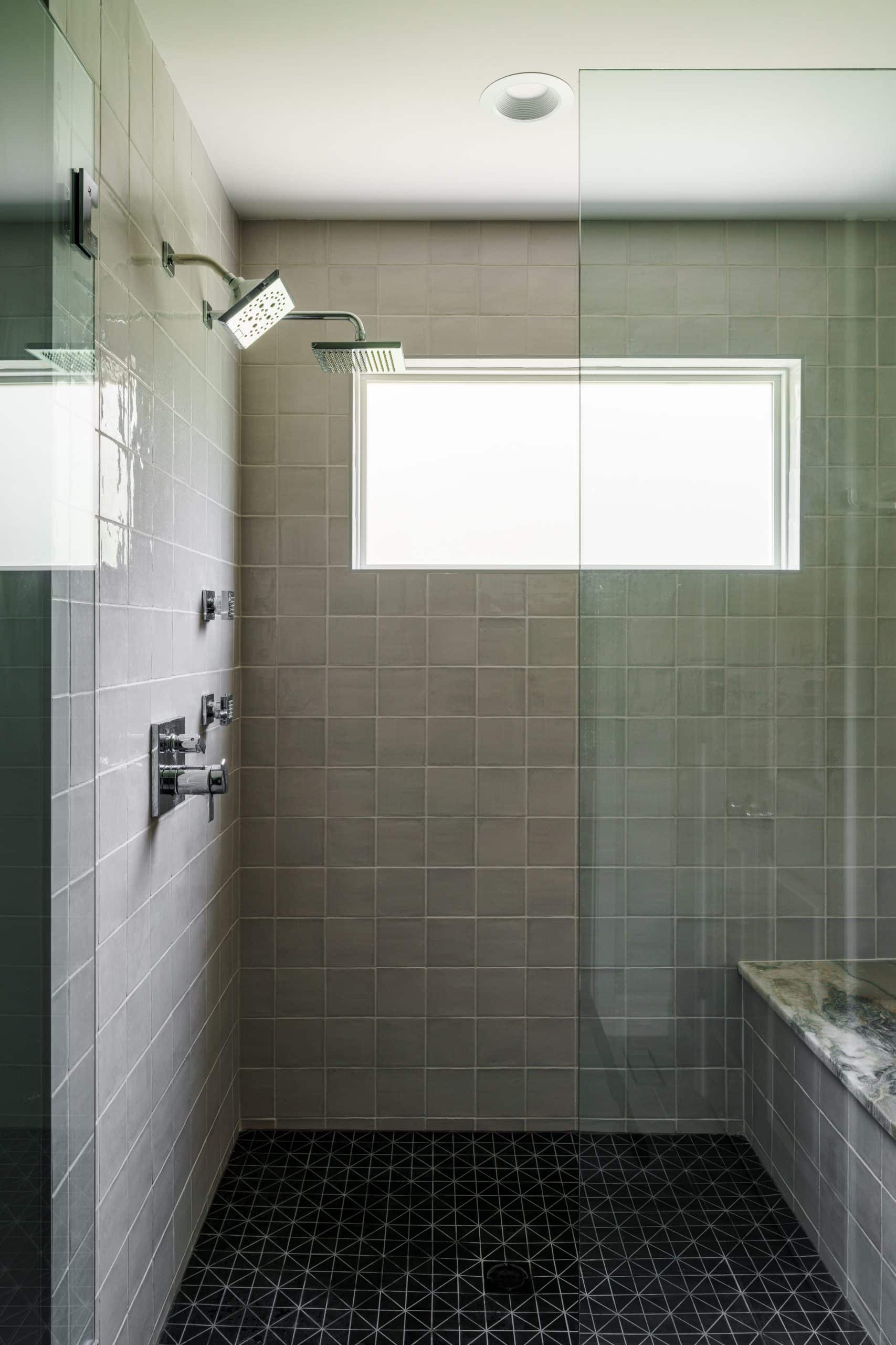 Kansas City bathroom remodeling featuring a modern, spa-like shower with dual shower heads, a glass enclosure, and a gray stone bench for a luxury home remodel.