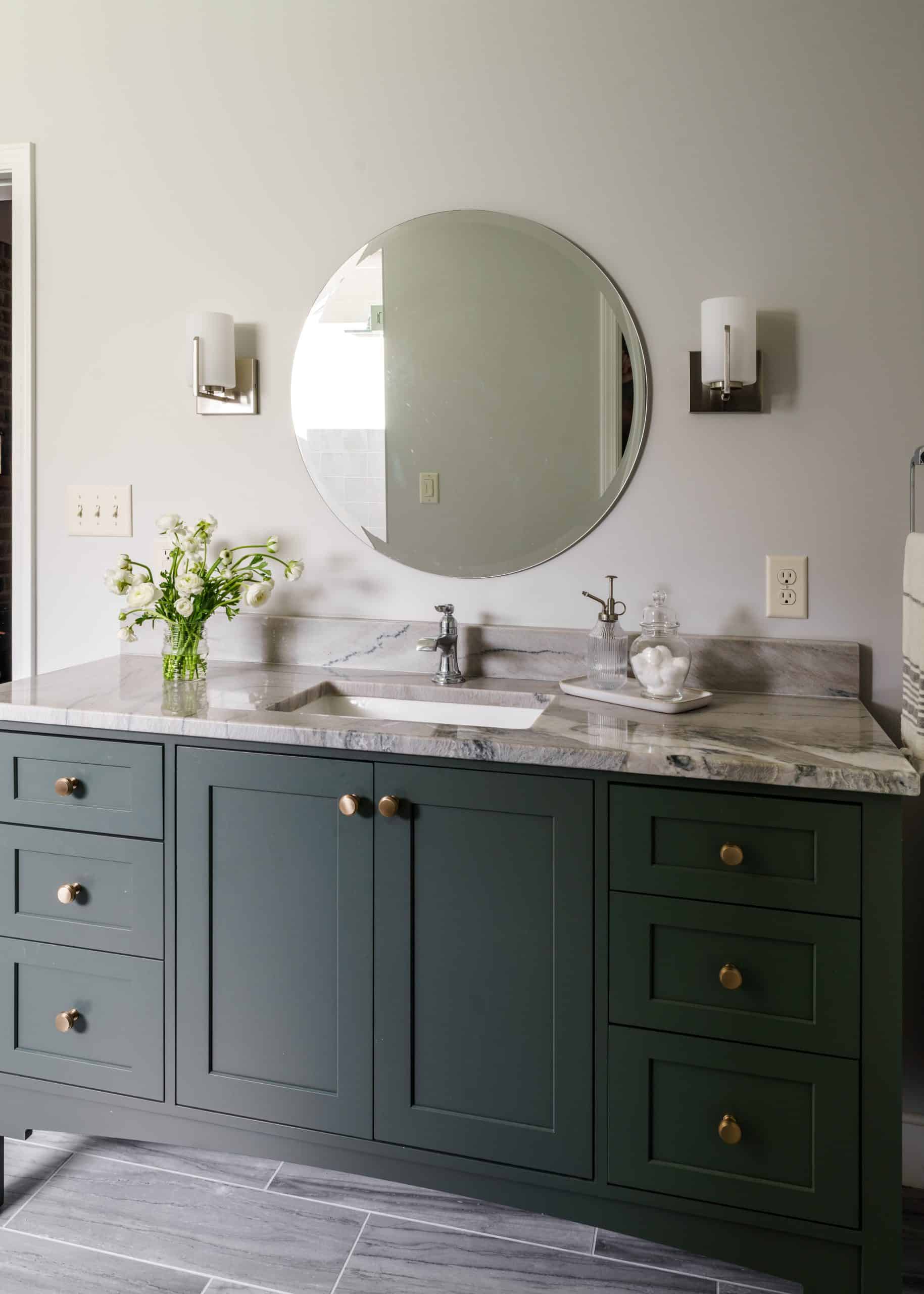 Kansas City bathroom remodel featuring a custom green vanity with a natural stone counter, polished brass knobs, and modern sconces, perfect for upscale home remodeling.