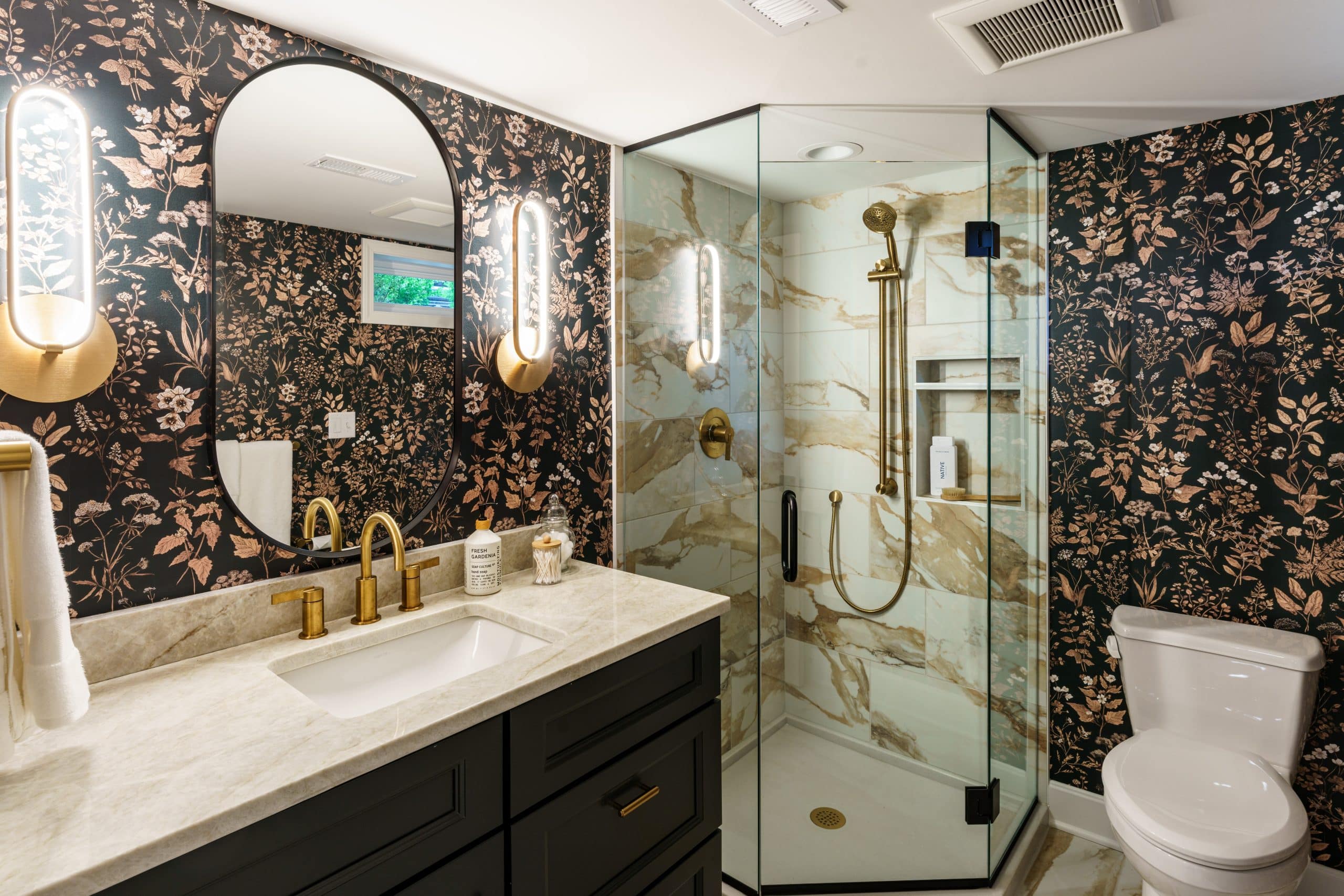 modern glam statement bathroom in prairie village basement remodel featuring black floral wallpaper and dramatic gold accents