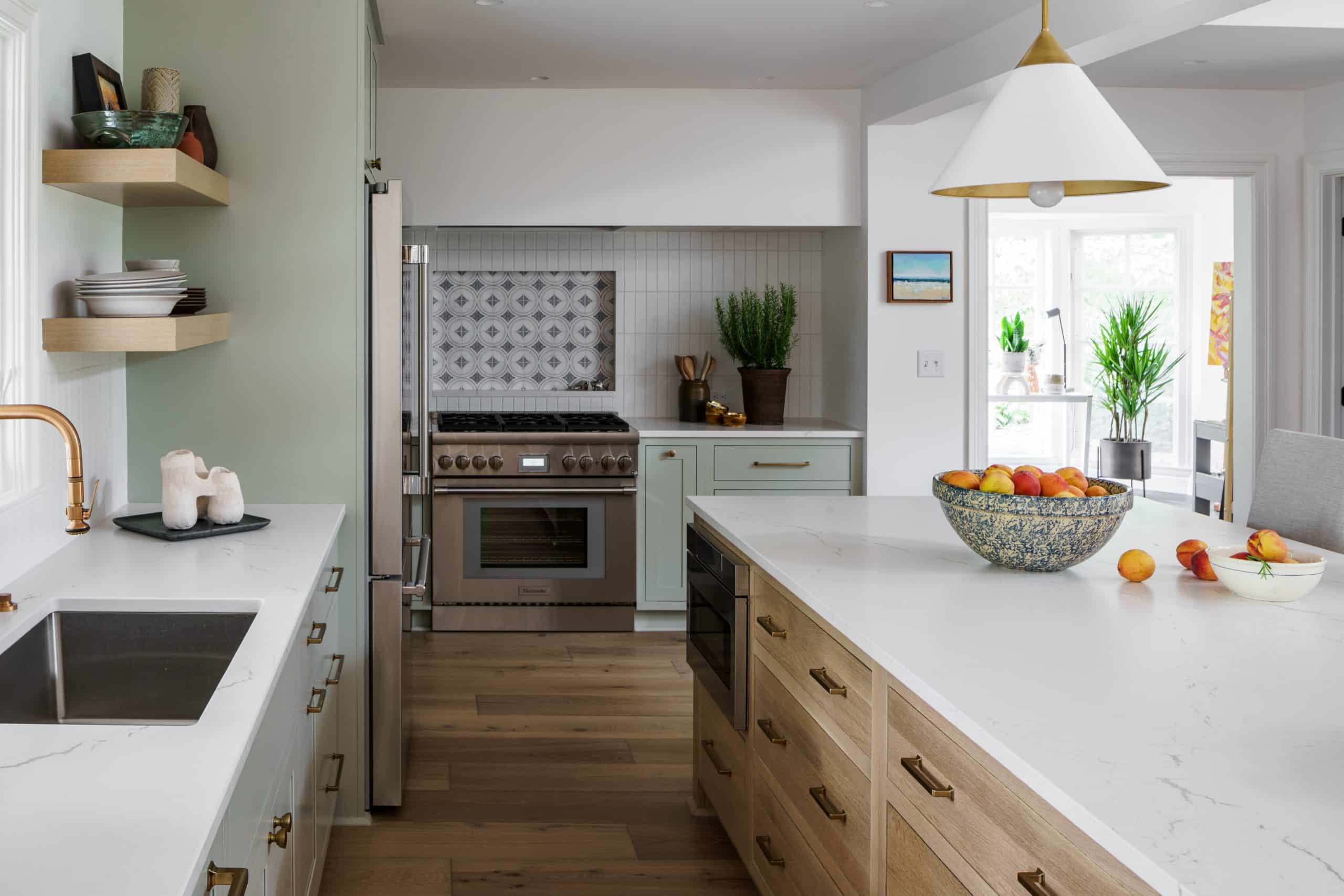 Bright kitchen renovation with sage green lower cabinets, white Cambria island countertop, open wood shelving, and polished brass fixtures in a KC home.