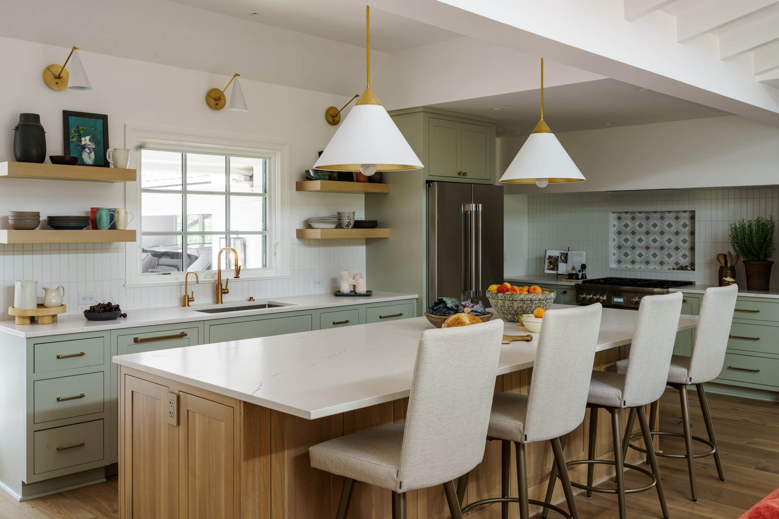 Bright kitchen renovation with sage green lower cabinets, white Cambria island countertop, open wood shelving, and polished brass fixtures in a KC home.