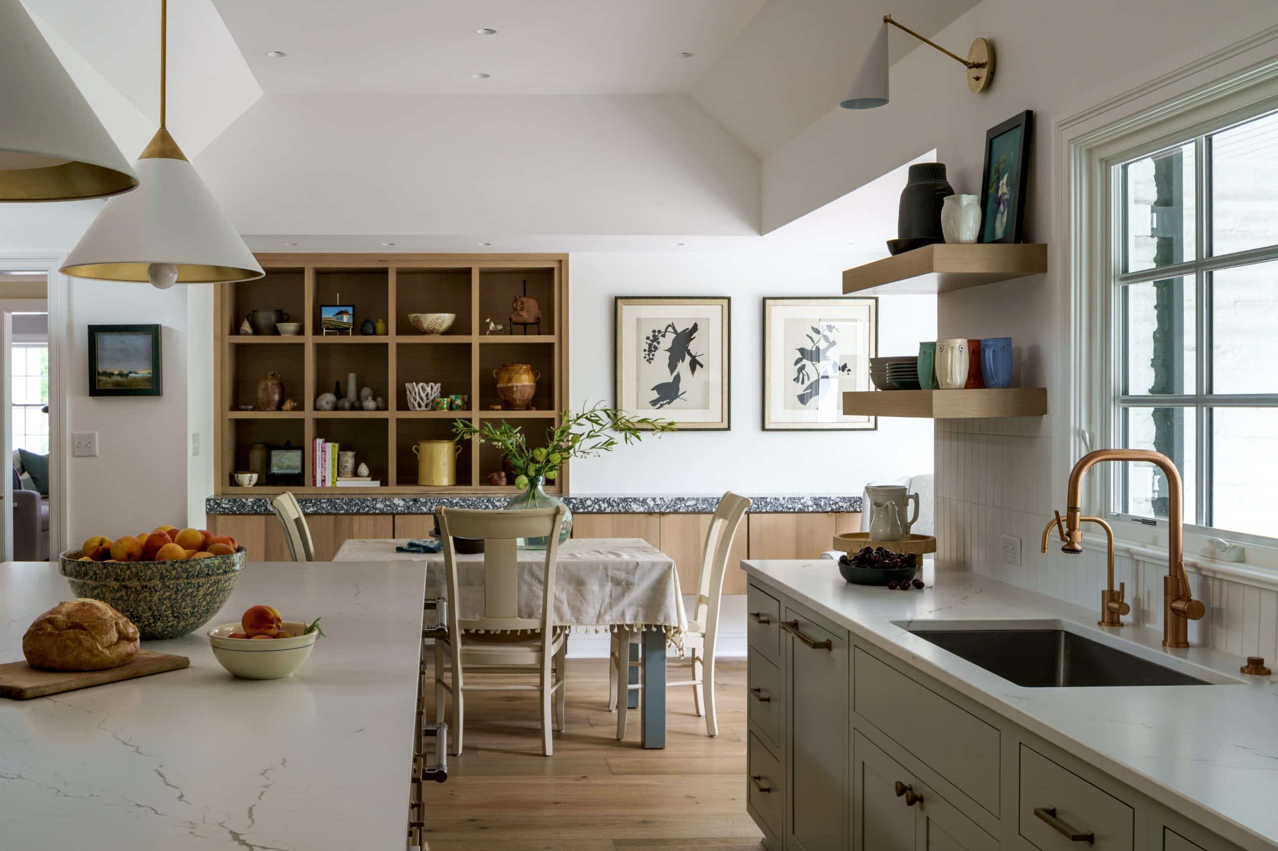  Light sage green lower cabinets, white Cambria quartz countertops, subtle white tile backsplash, and wood floating shelves with gold sconces.