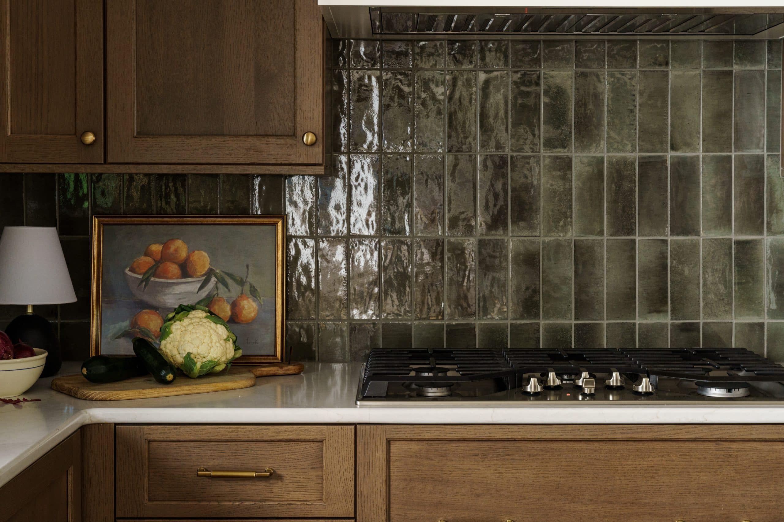  Close-up of upscale kitchen backsplash featuring high-gloss, handmade-look olive green subway tile over a gas range, contrasting with warm wood cabinetry in a Kansas City remodel.