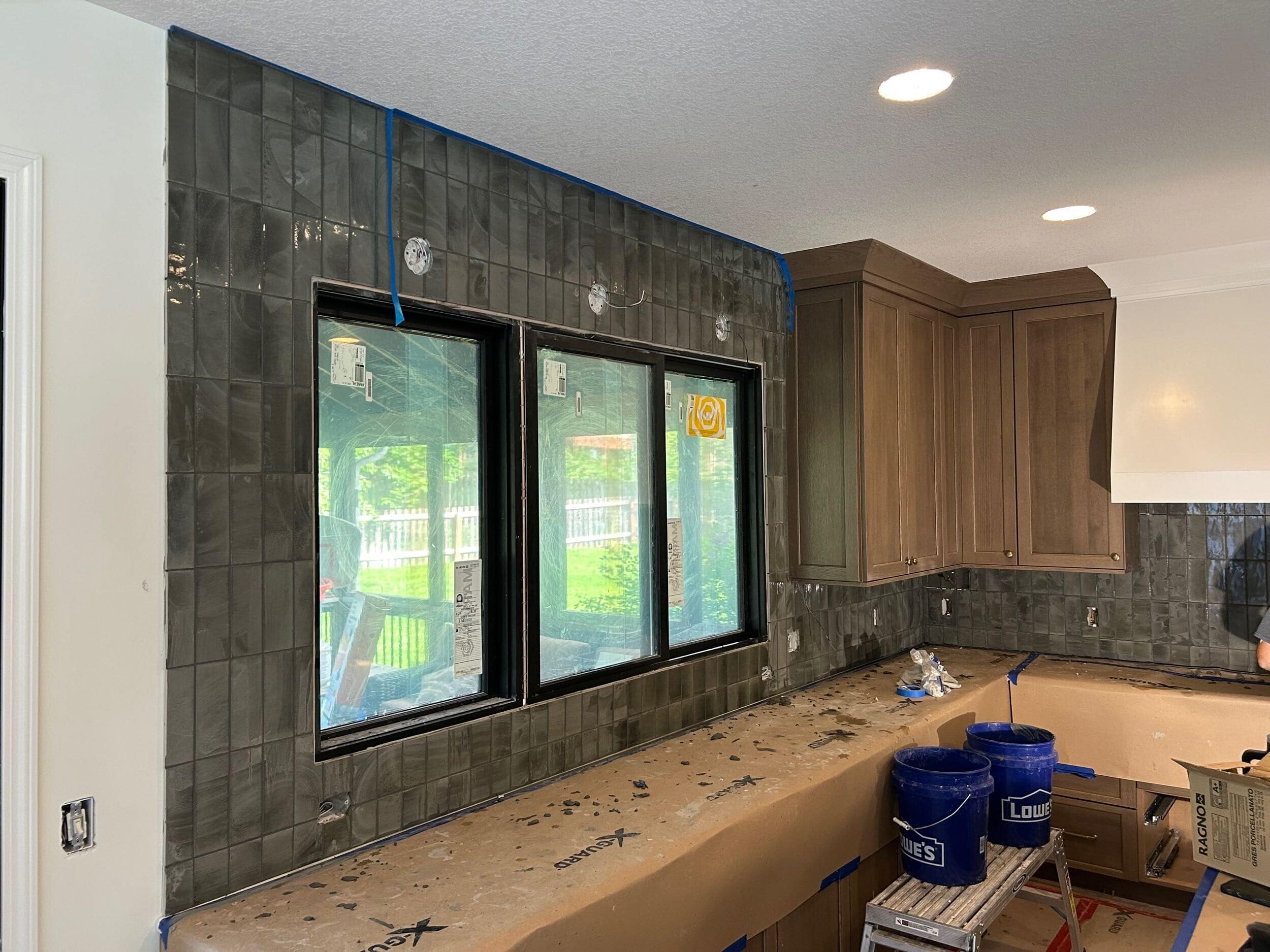 the moody sleek olive green subway tile being installed from counter to ceiling in this overland park ks kitchen remodel with schloegel design remodel