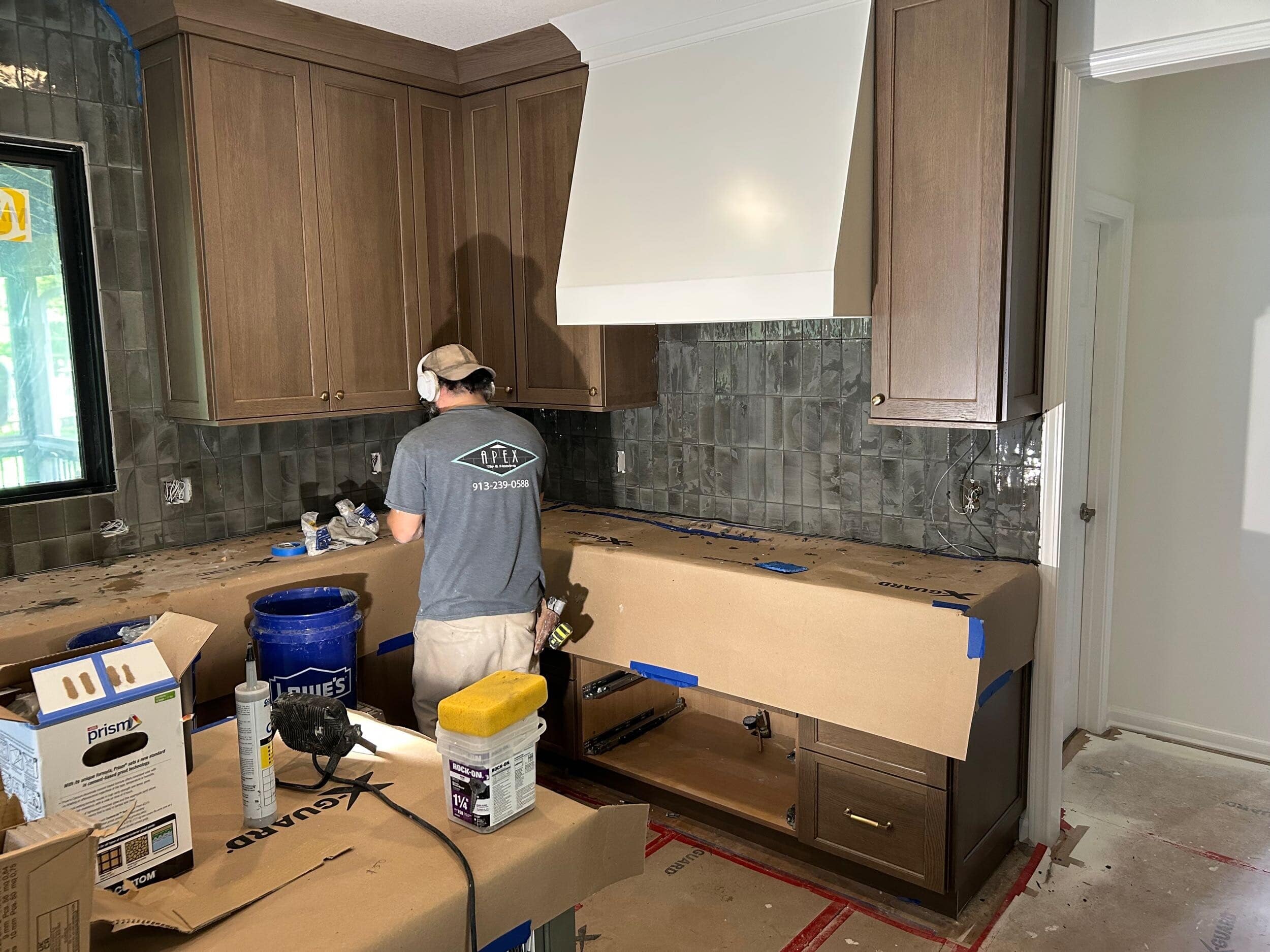 the moody sleek olive green subway tile being installed from counter to ceiling in this overland park ks kitchen remodel with schloegel design remodel