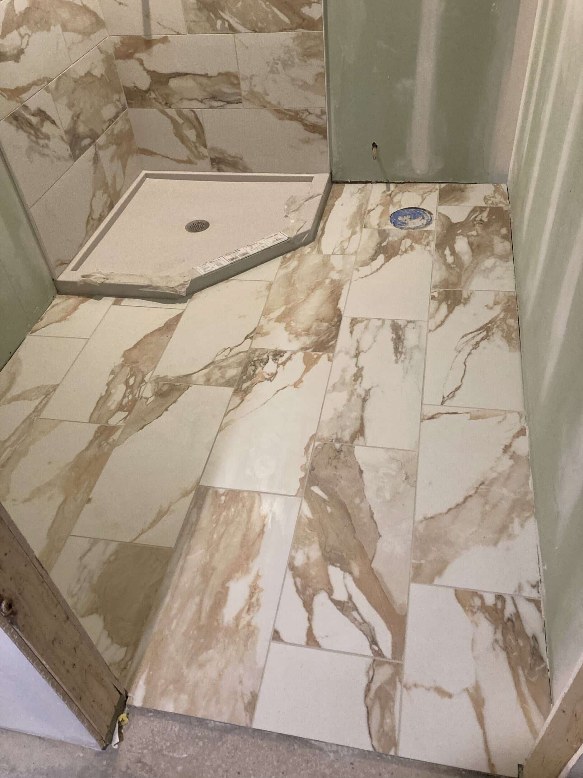 bathroom tile being laid. same large format porcelain tile is used on the bathroom floor and shower walls. its creamy white with gold and beige toned large flowing veining. 