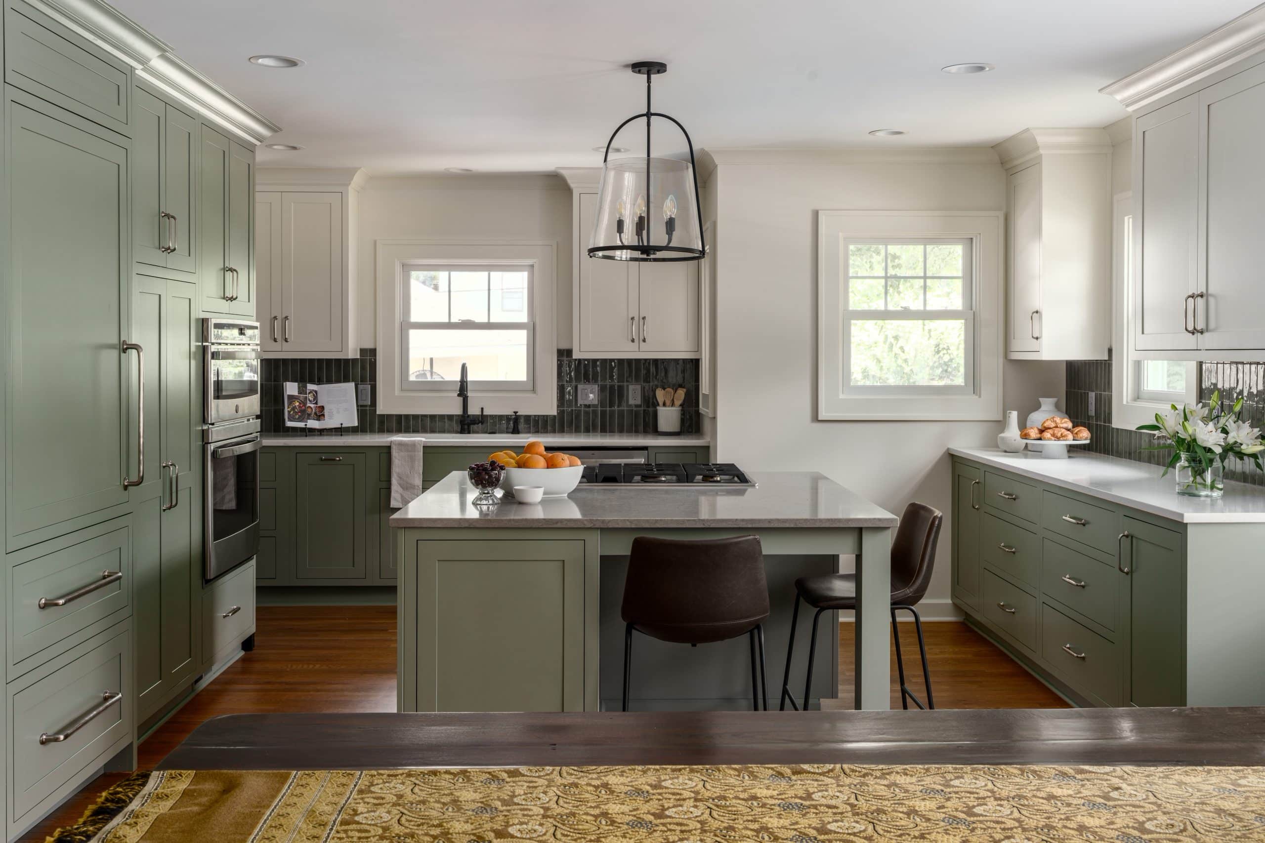 view into newly remodeled timeless kitchen with large island and integrated luxury appliances and light sage green bottom cabinets and creamy white uppers