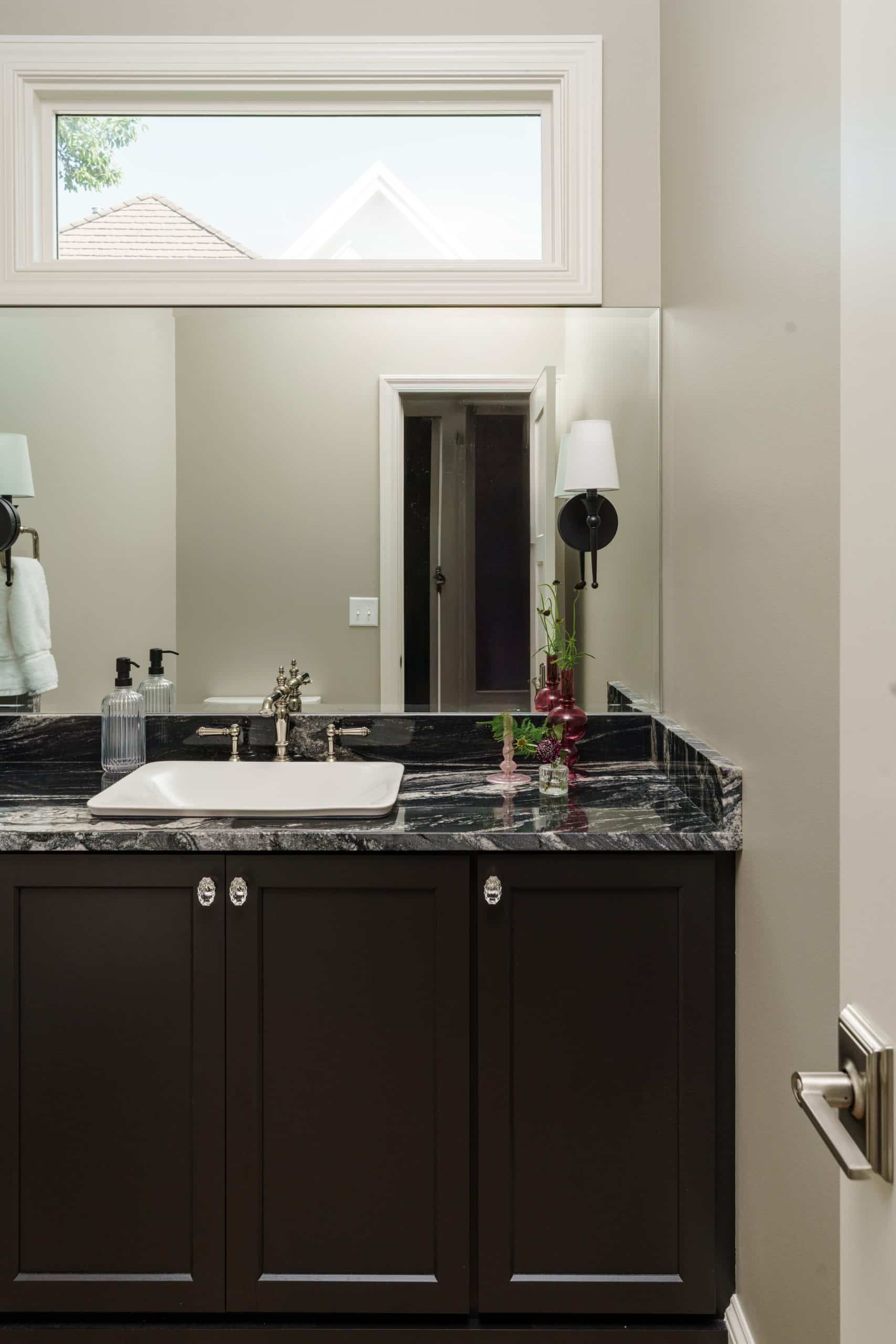 moody dark almost black custom cabinetry with black quartz and traditional sconces with art deco vintage inspired clear cabinet pulls