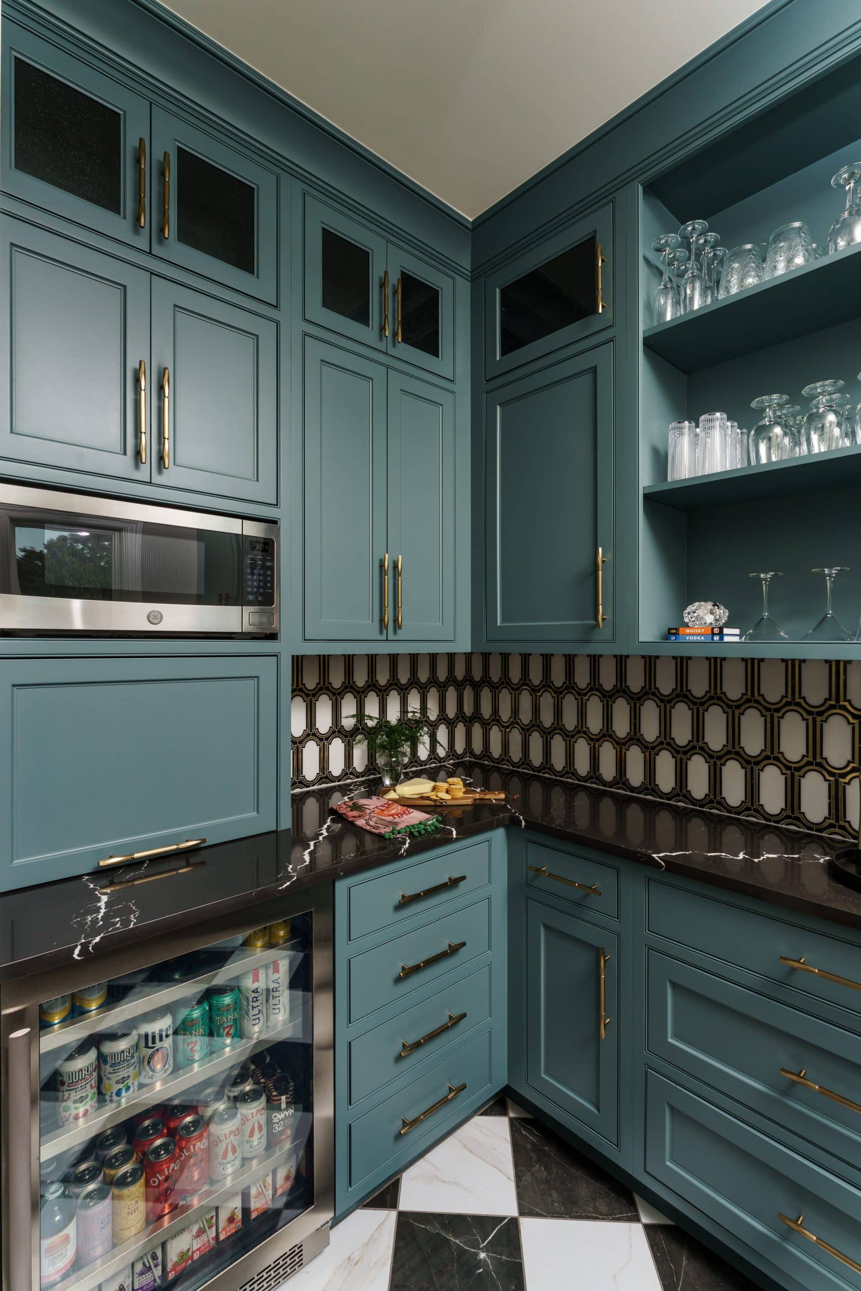 moody statement art deco inspired butler's pantry with deep teal cabinetry and black and white checkered floor tile and gold and white patterned backsplash tile