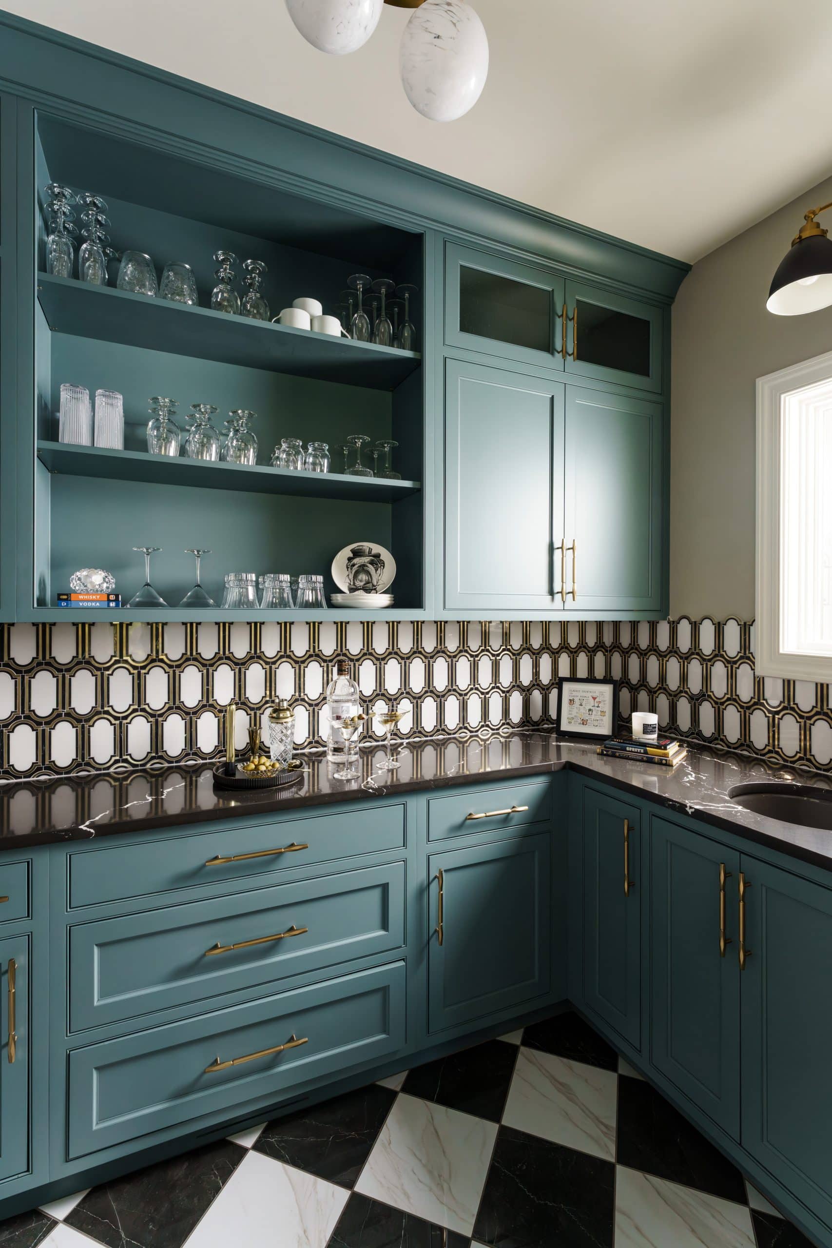 moody statement art deco inspired butler's pantry with deep teal cabinetry and black and white checkered floor tile and gold and white patterned backsplash tile