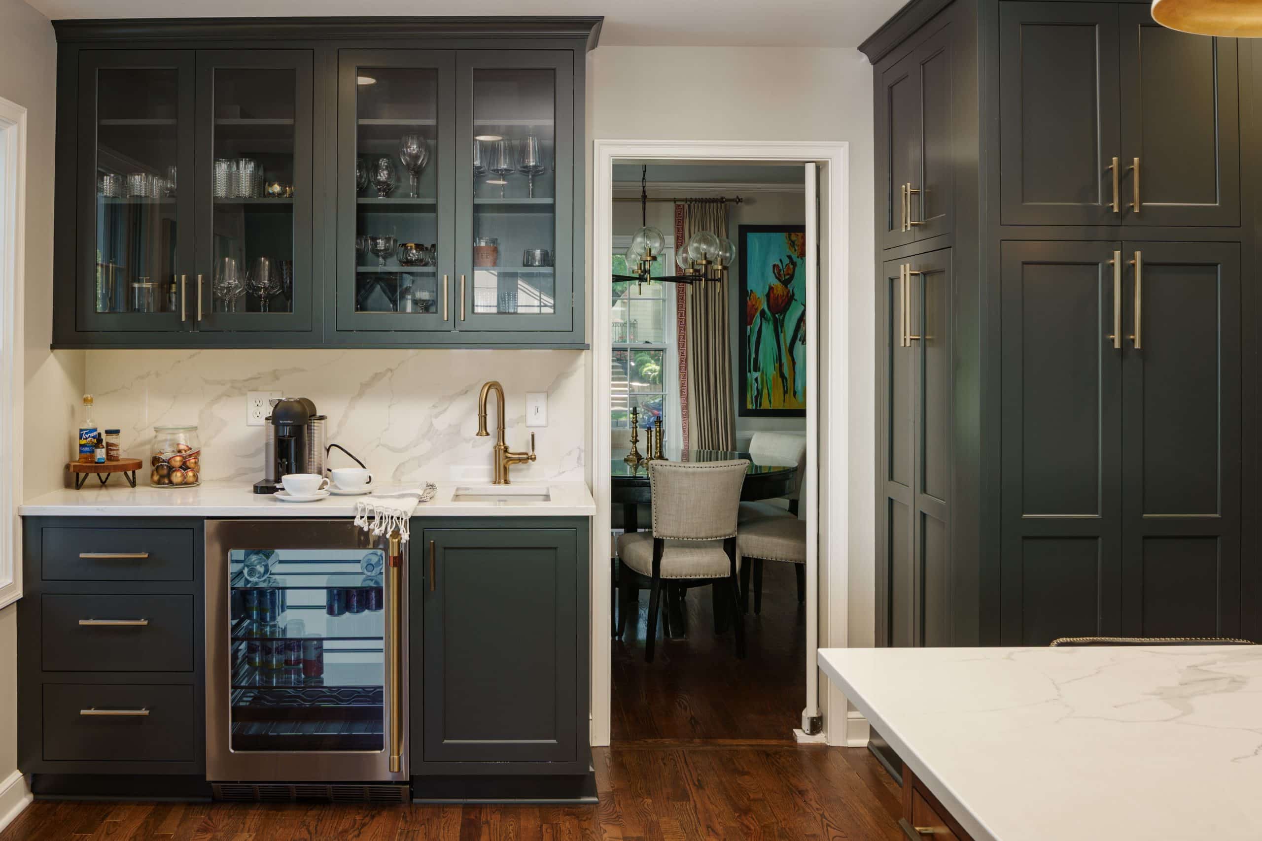Brookside kitchen beverage bar Detail of the Brookside kitchen featuring a custom beverage station with deep grey shaker cabinetry, brass fixtures, quartz countertops and backsplash, glass display cabinets, and built-in beverage refrigerator, blending modern personality with classic craftsmanship.