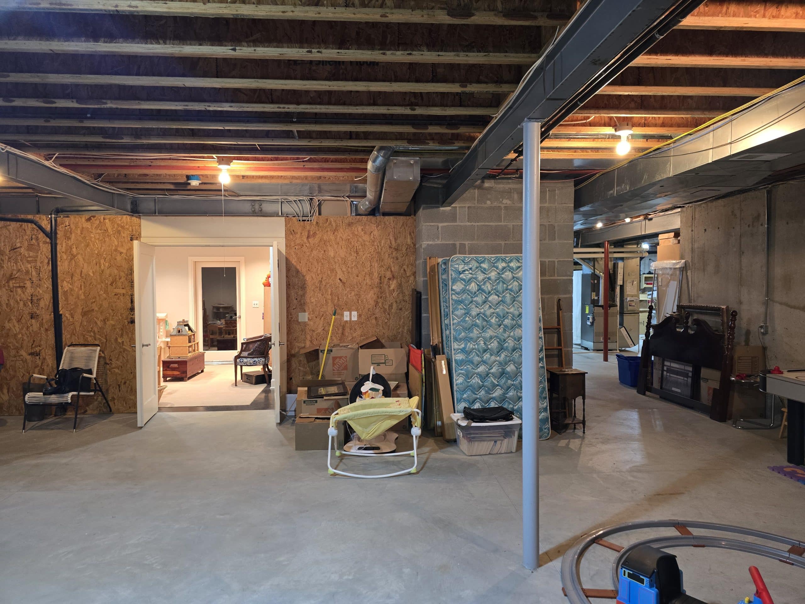 Unfinished basement with cement floors and exposed beams before remodel