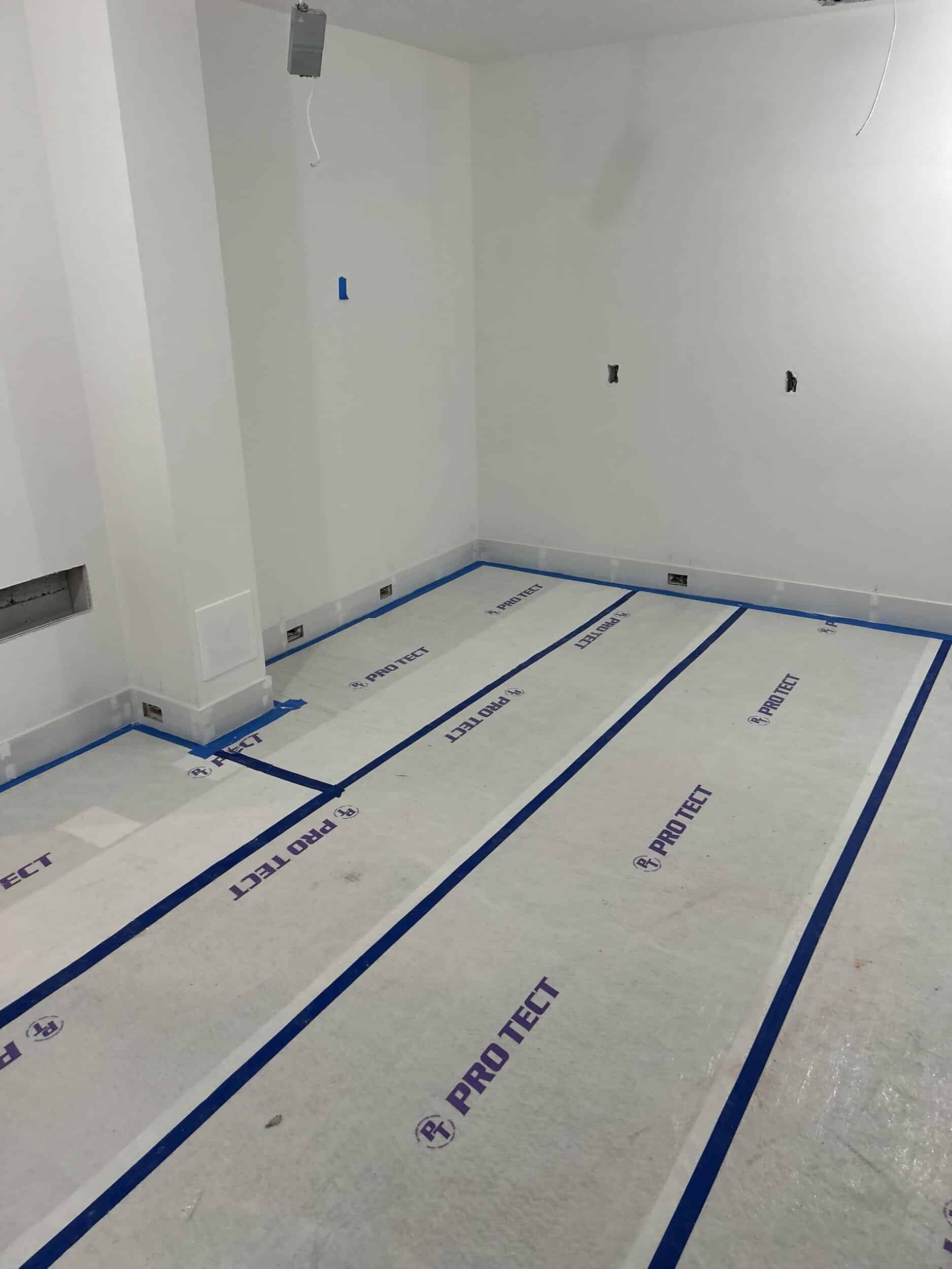 new LVP flooring installed in home basement gym remodel in Cedar Creek, Olathe with white oak finish and looks like real hardwoods and now covered over with white floor protection sheets and taped down 
