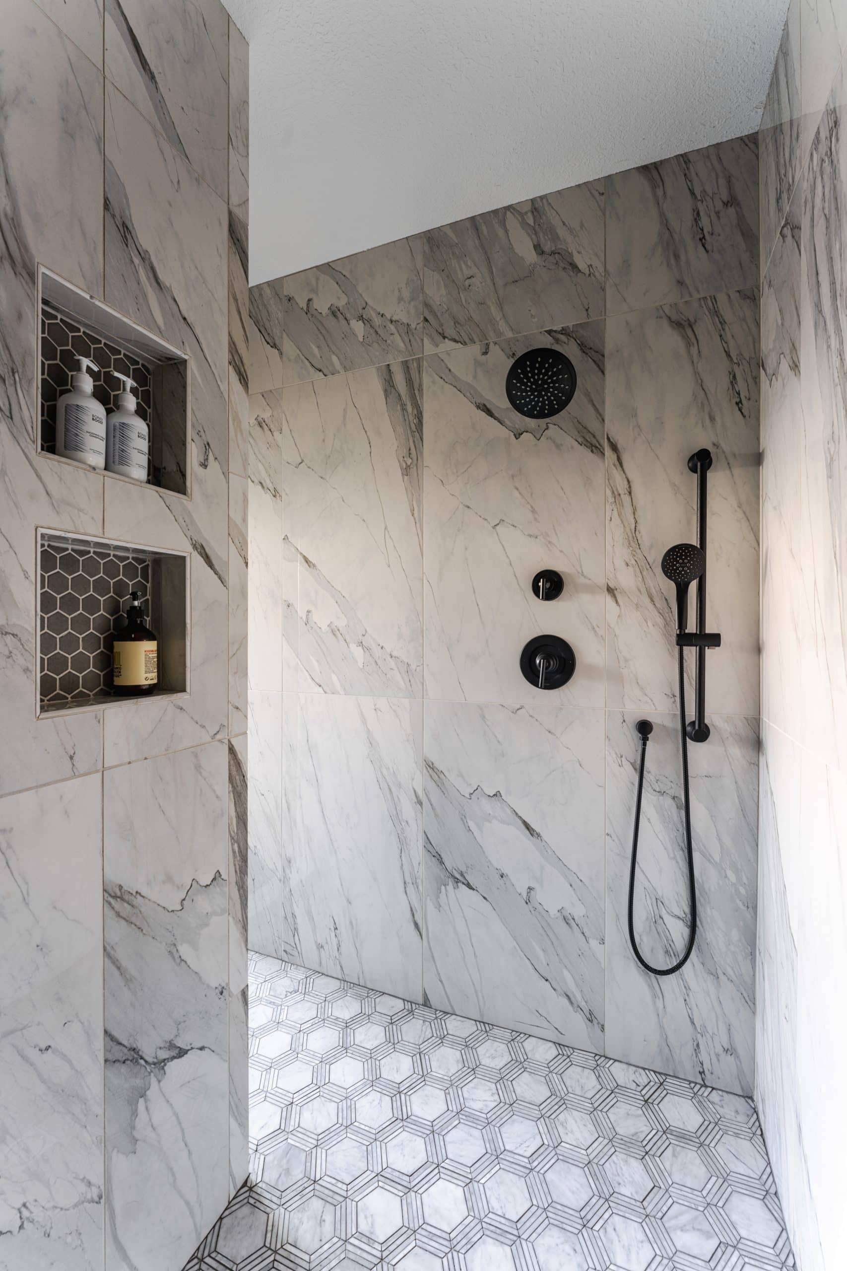walk-in shower with two niches and multiple shower heads and hand held shower head and marble inspired tile in spa-like primary bathroom remodel walk-in shower with two niches and multiple shower heads and hand held shower head and marble inspired tile in spa-like primary bathroom remodel