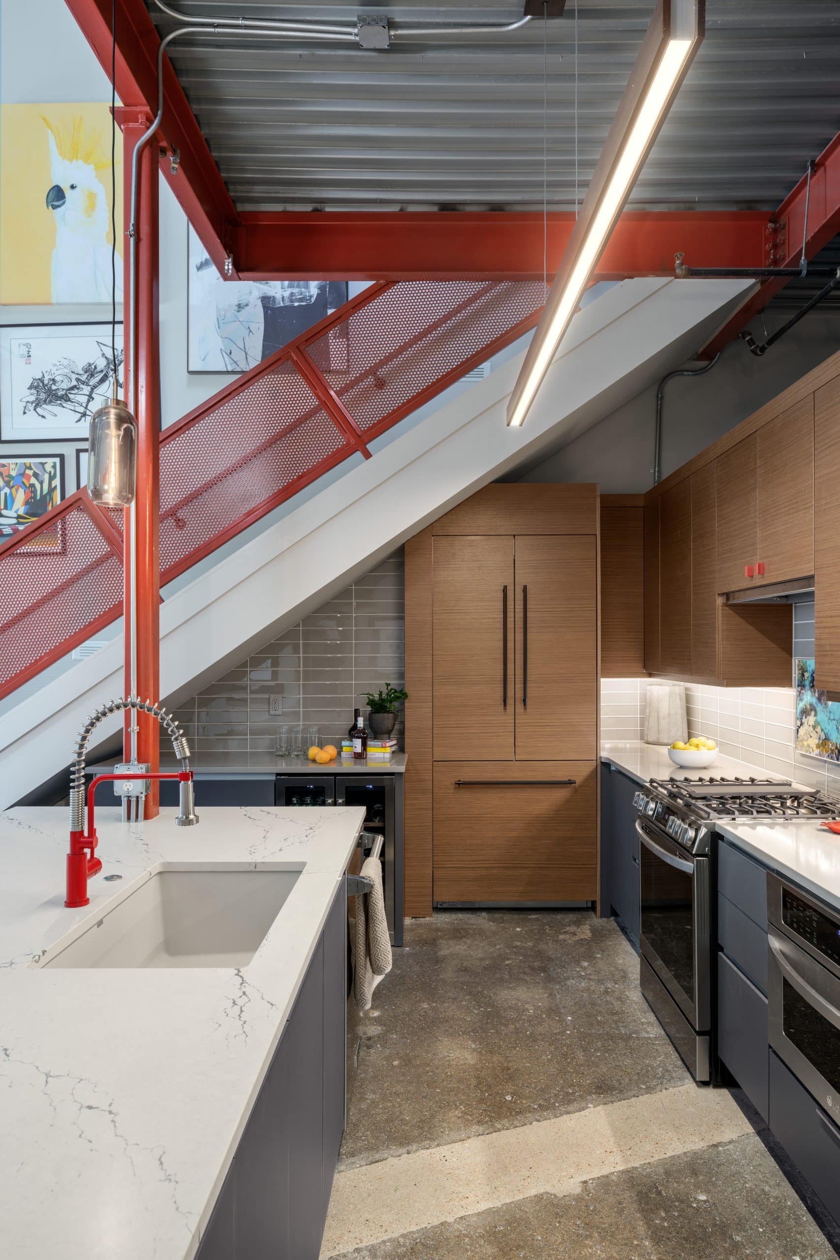 Contemporary Kansas City condo kitchen with large island, quartz countertop, wood cabinetry and red faucet Contemporary Kansas City condo kitchen with large island, quartz countertop, wood cabinetry and red faucet